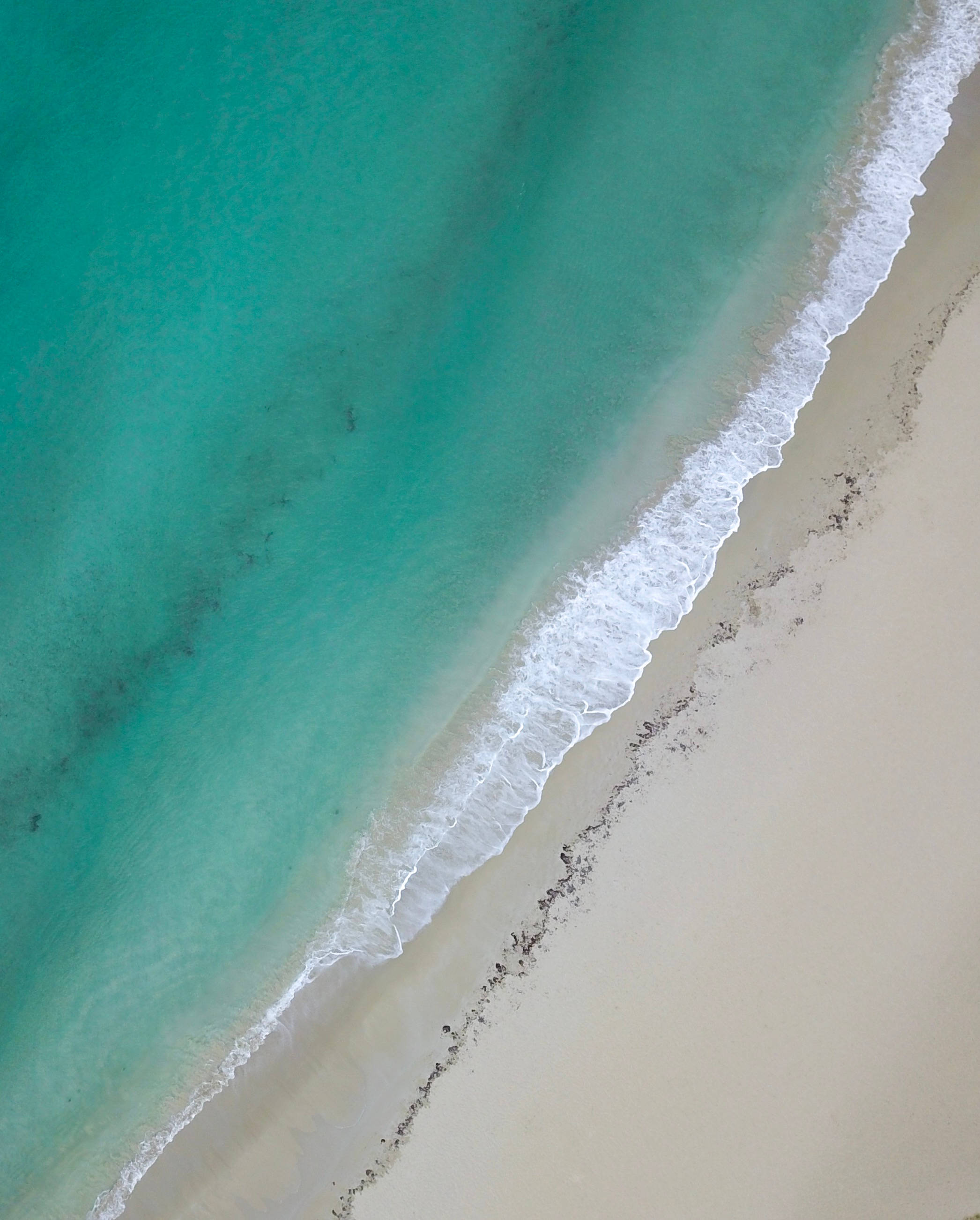 寧靜邦迪海灘澳洲 iPhone 背景 壁紙 — 從高空俯瞰，藍綠色海浪以對角線輕輕拍打淡色沙灘。