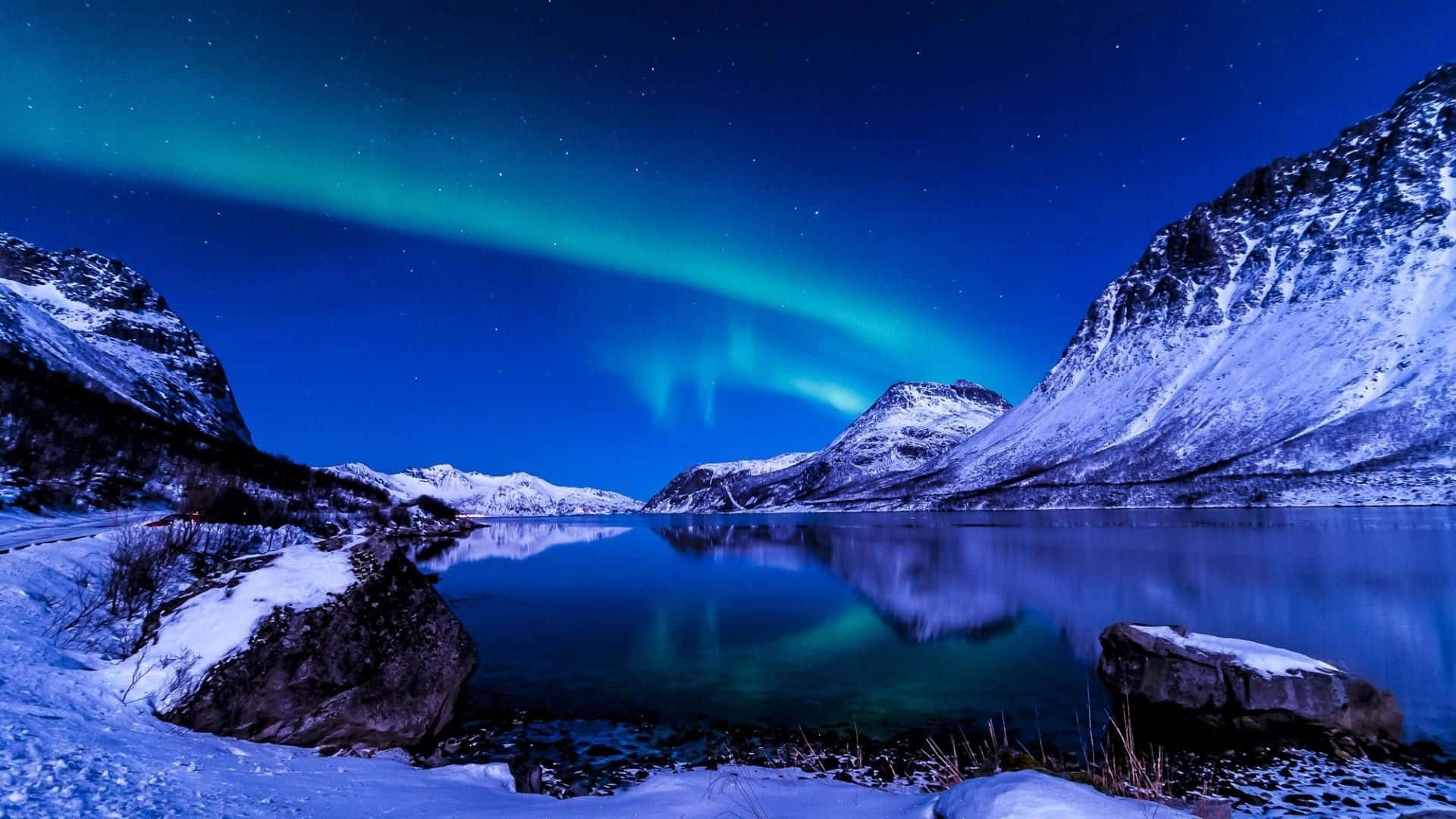 北極光照耀在積雪的山脈和寧靜的湖面上。