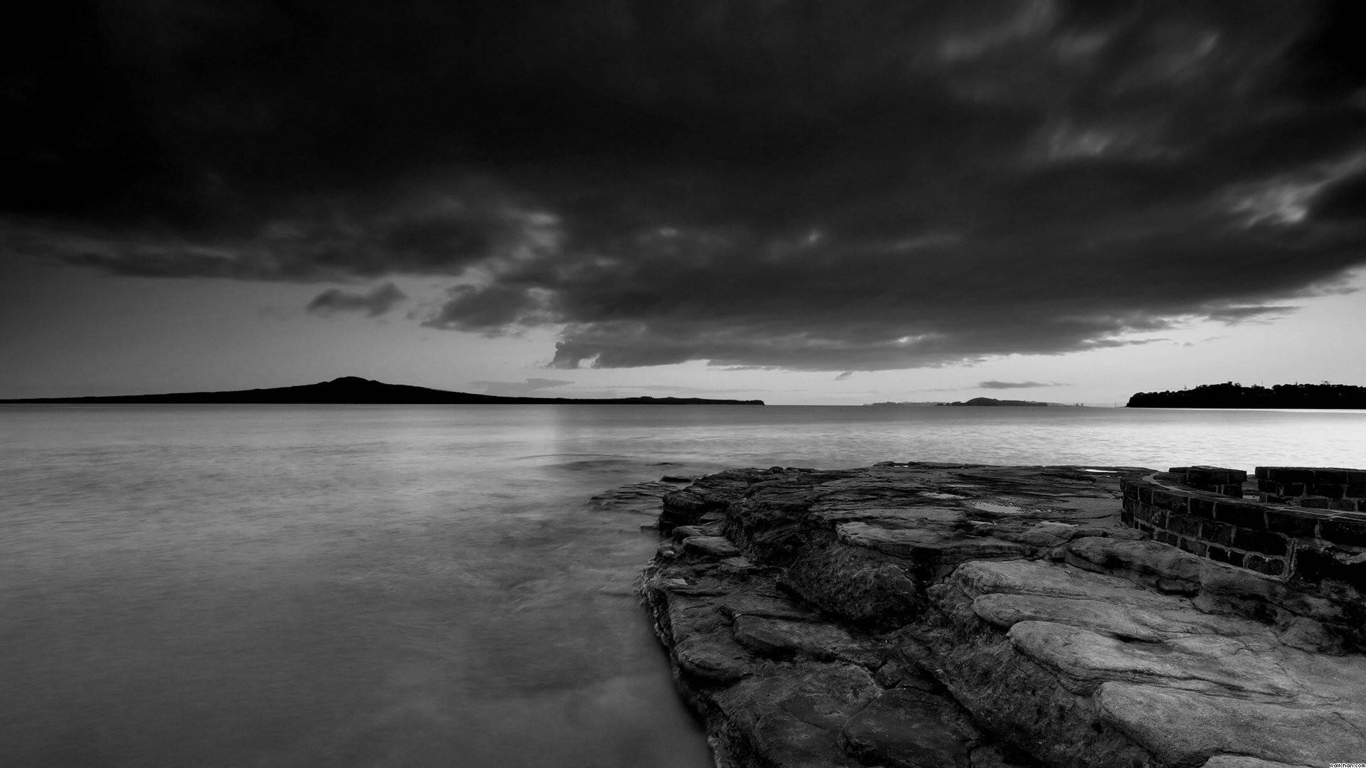 寧靜黑白海景 壁紙 — 在黃昏時分，戲劇性的暴風雲下，岩石海岸線的陰鬱黑白長時間曝光。