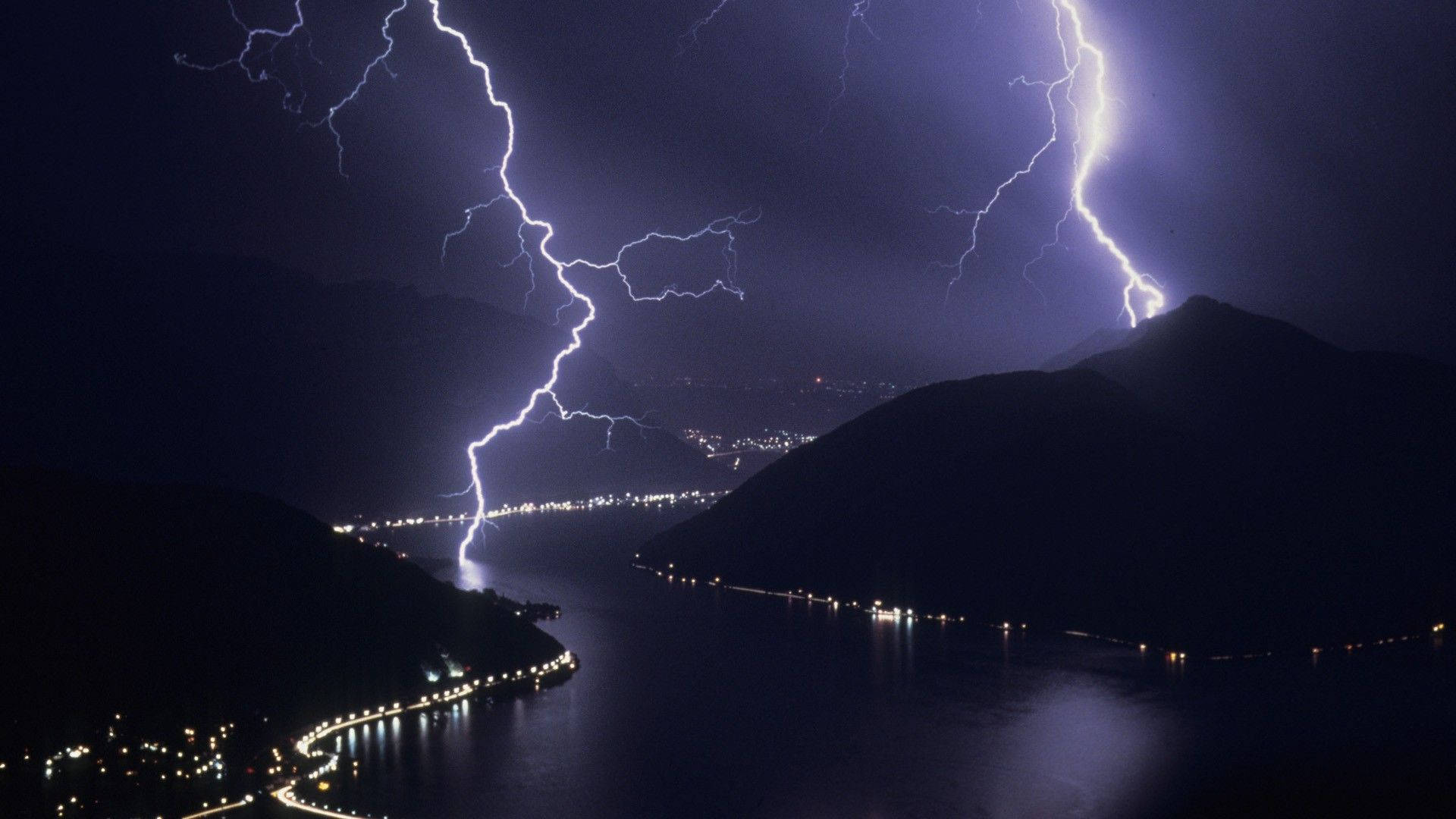 夜晚，山湖上空閃電，岸邊城市燈光閃爍。