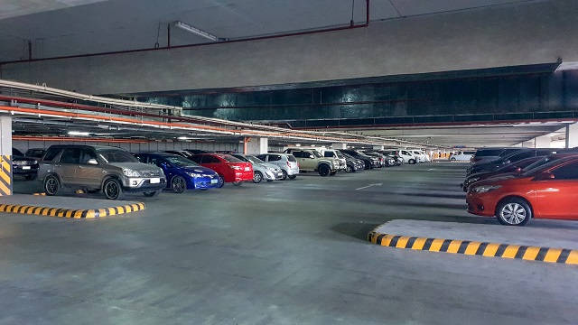 一排排停泊的汽車，位於帶有條紋路緣的混凝土地下停車場。
