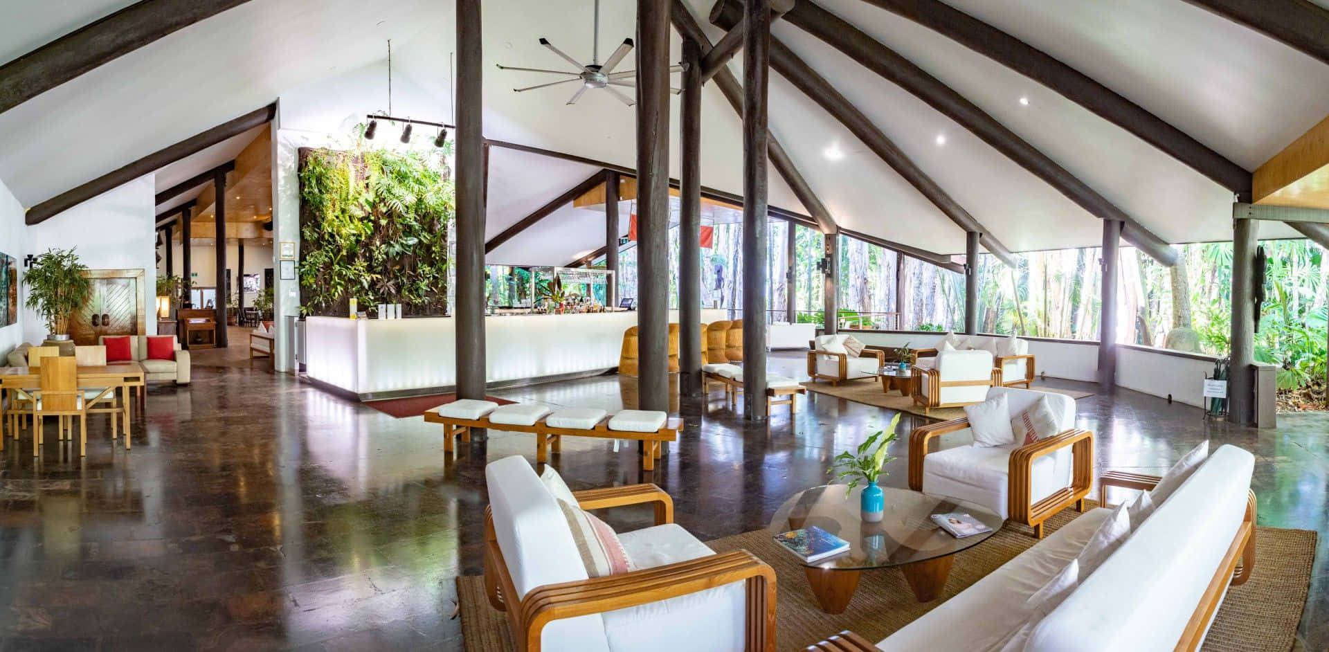 Beach Resort 桌布 壁紙 — 寬敞的熱帶度假村大堂，設有木樑、拋光地板，透過大窗戶可欣賞茂密的綠植。