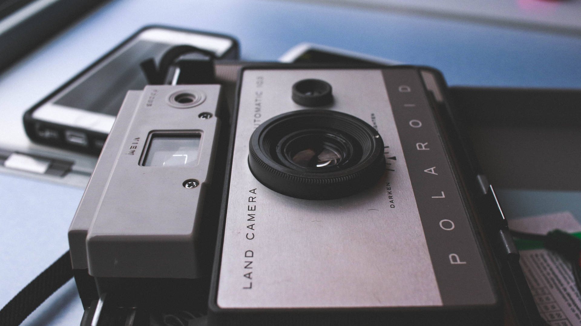 復古Polaroid相機放在藍色桌子上的智能手機旁邊。
