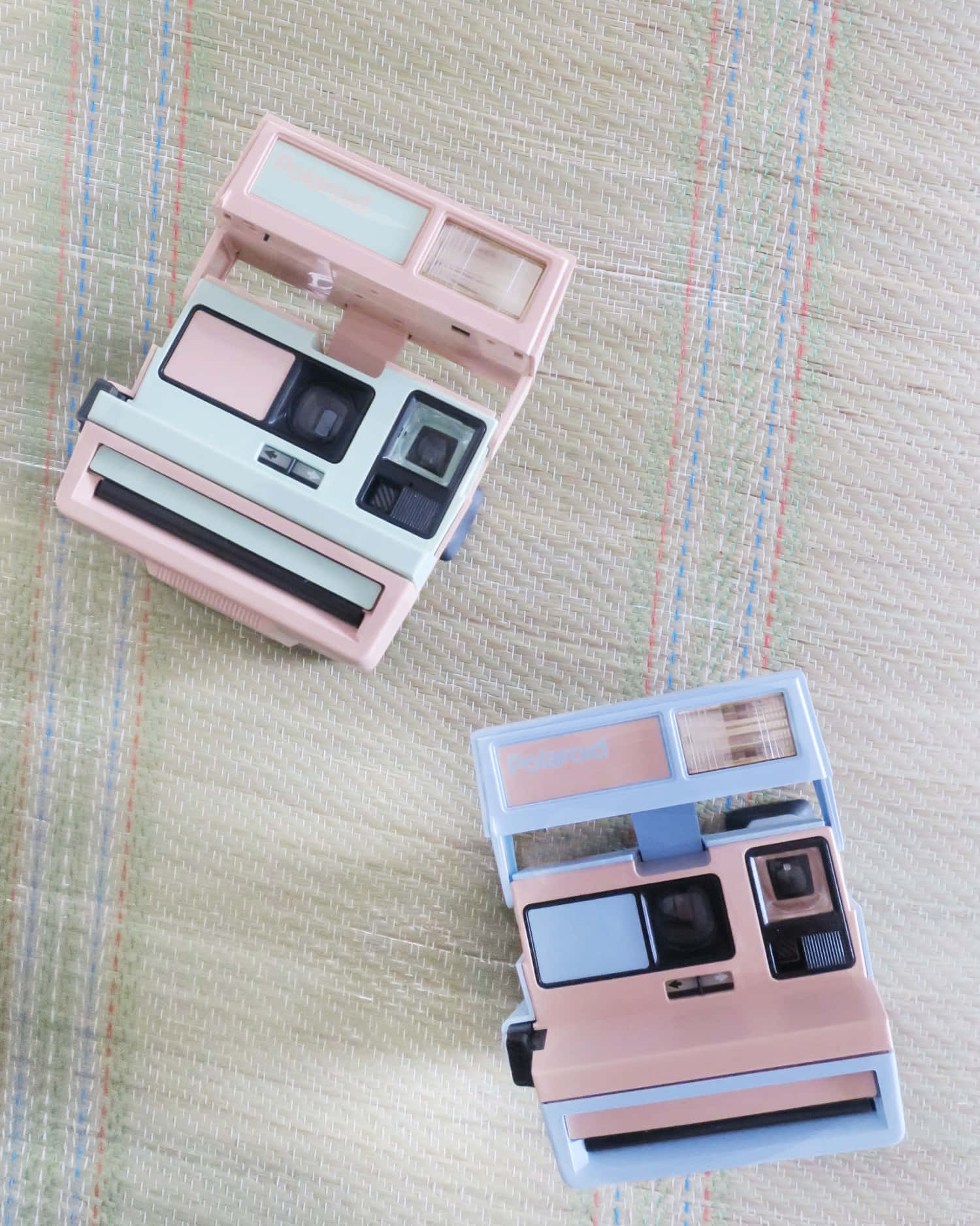 兩部粉彩色復古Polaroid相機喺一條紋編織表面上。