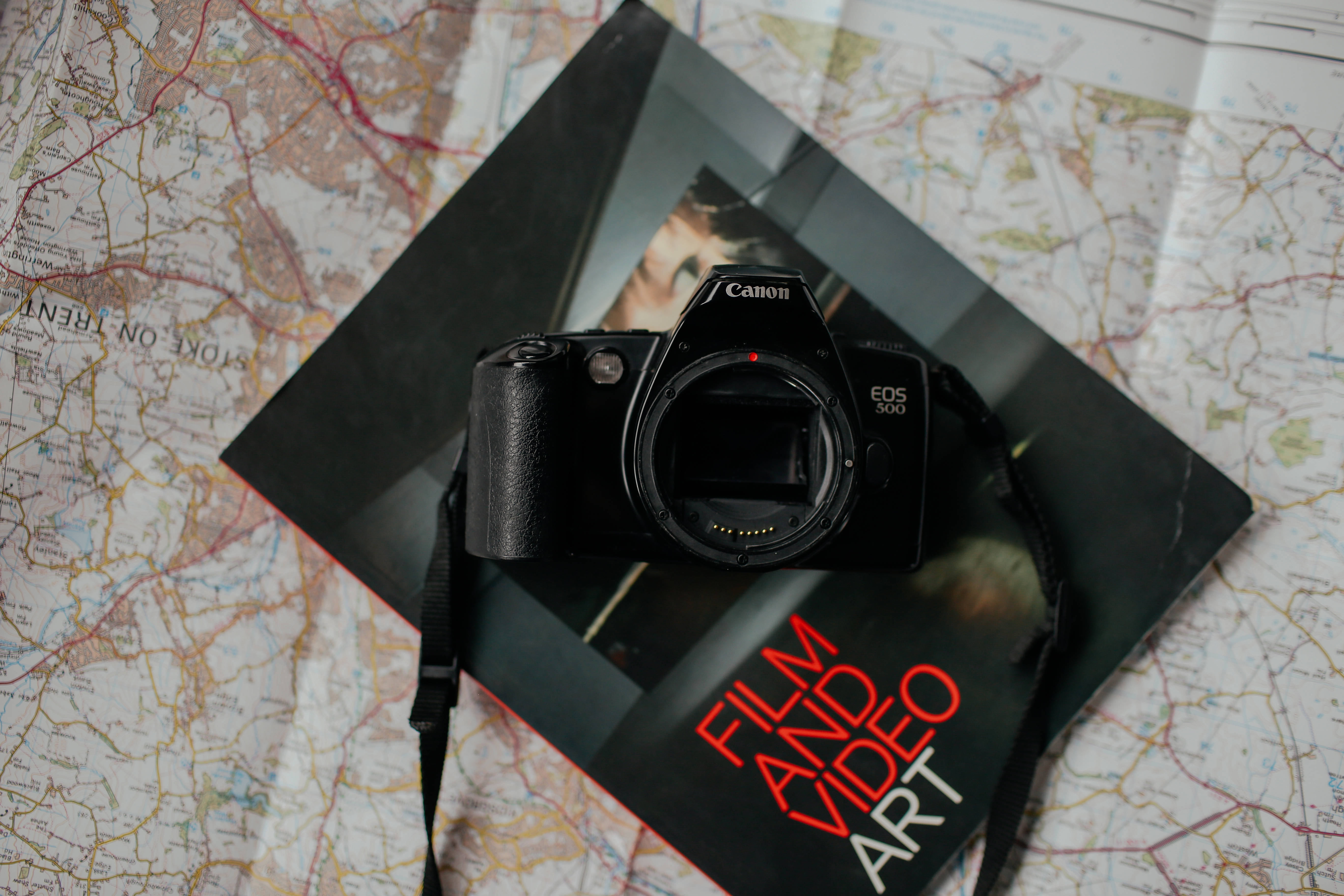 封面為黑色的雜誌配專業相機 壁紙 — 一部黑色 Canon EOS 300 DSLR 相機放在一本名為 'Film Video Art' 的書上，書本置於詳細的道路地圖上。