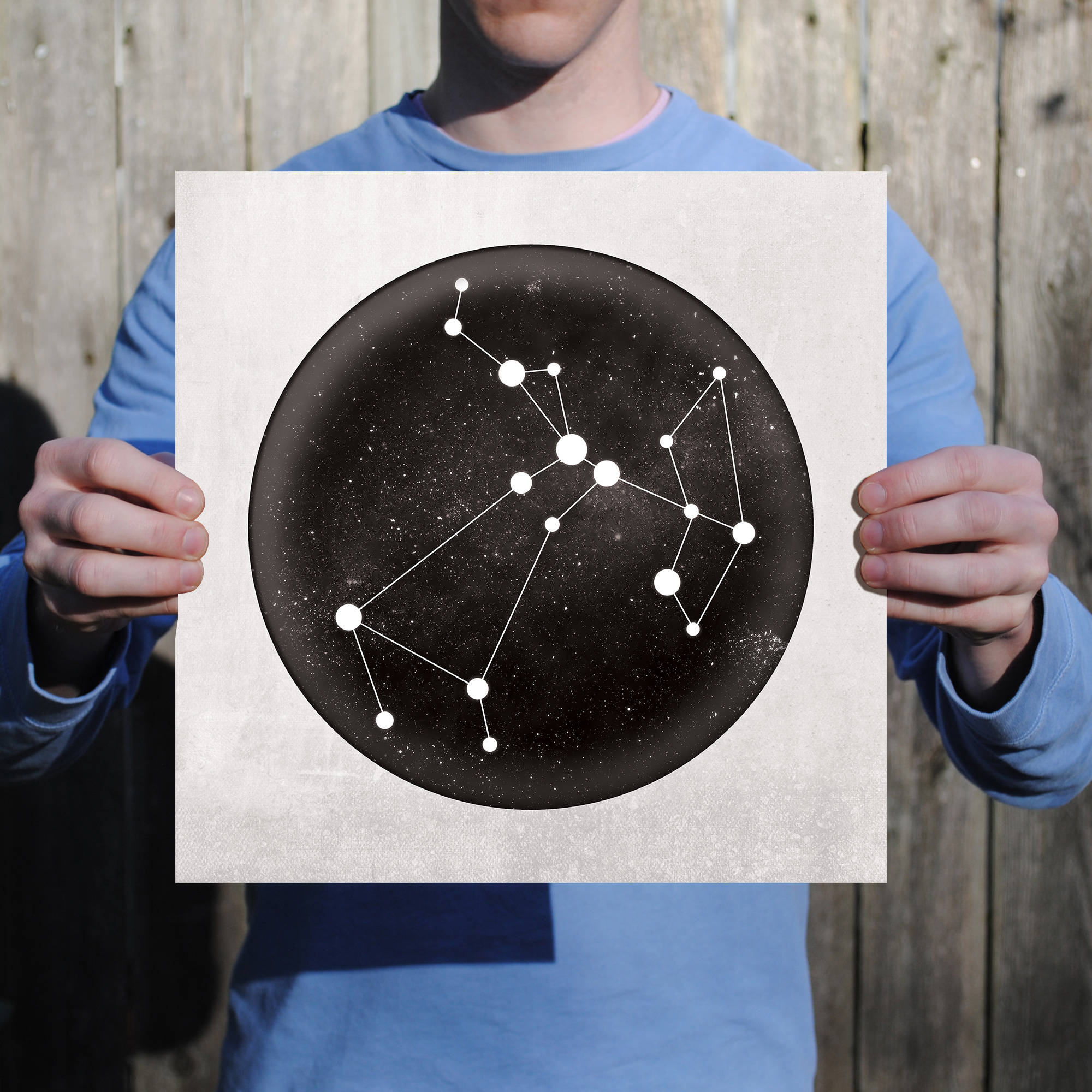 射手座星座星圖藝術 壁紙 — 一個人手持一張圓形海報，上面描繪了黑色星空背景上的白色線條星座，背景是木柵欄。