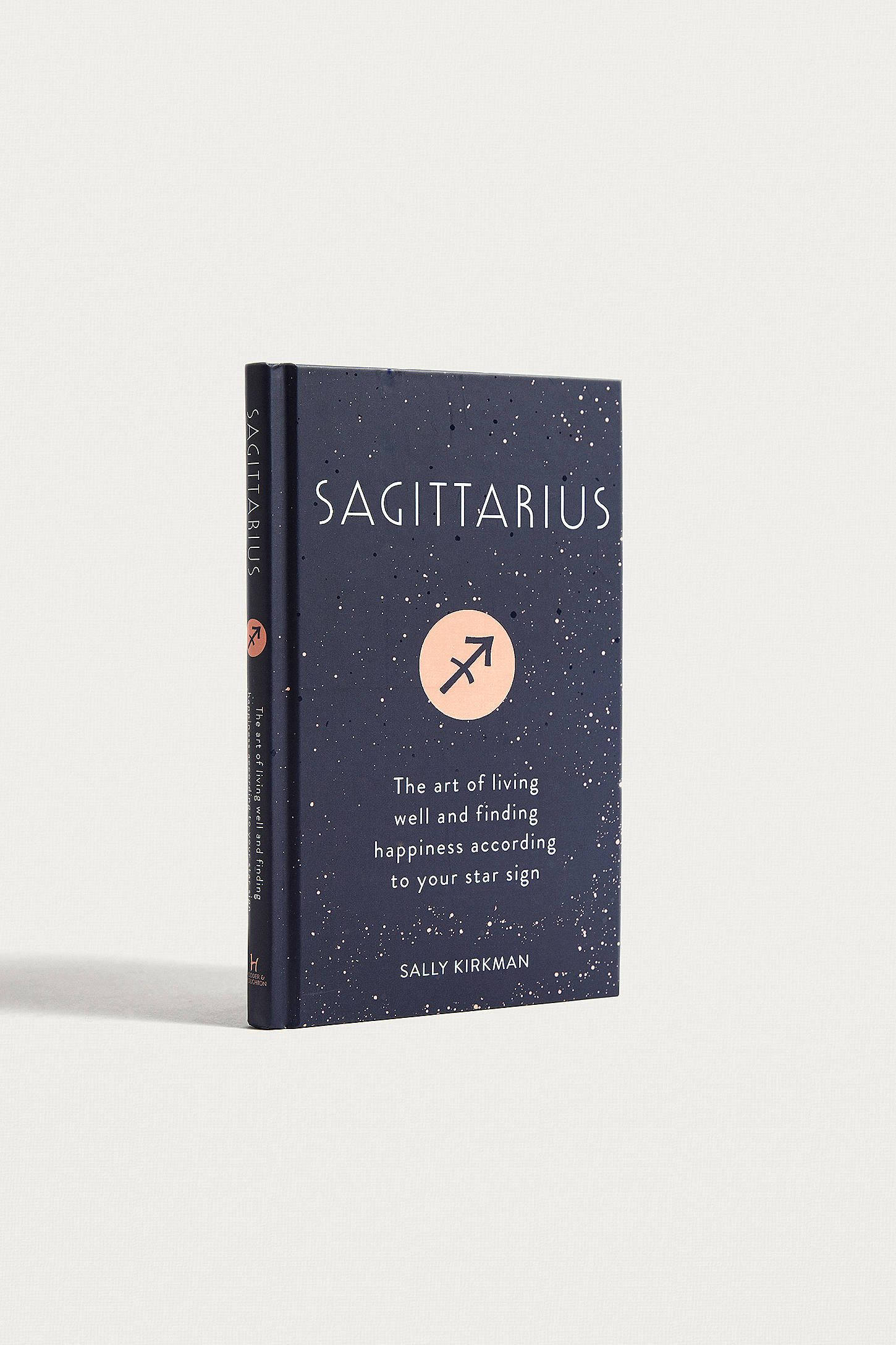 射手座星座書 壁紙 — 一本海軍藍色的書，書名為 Sagittarius，帶有星光封面和橙色箭頭符號，直立於純白色背景前。