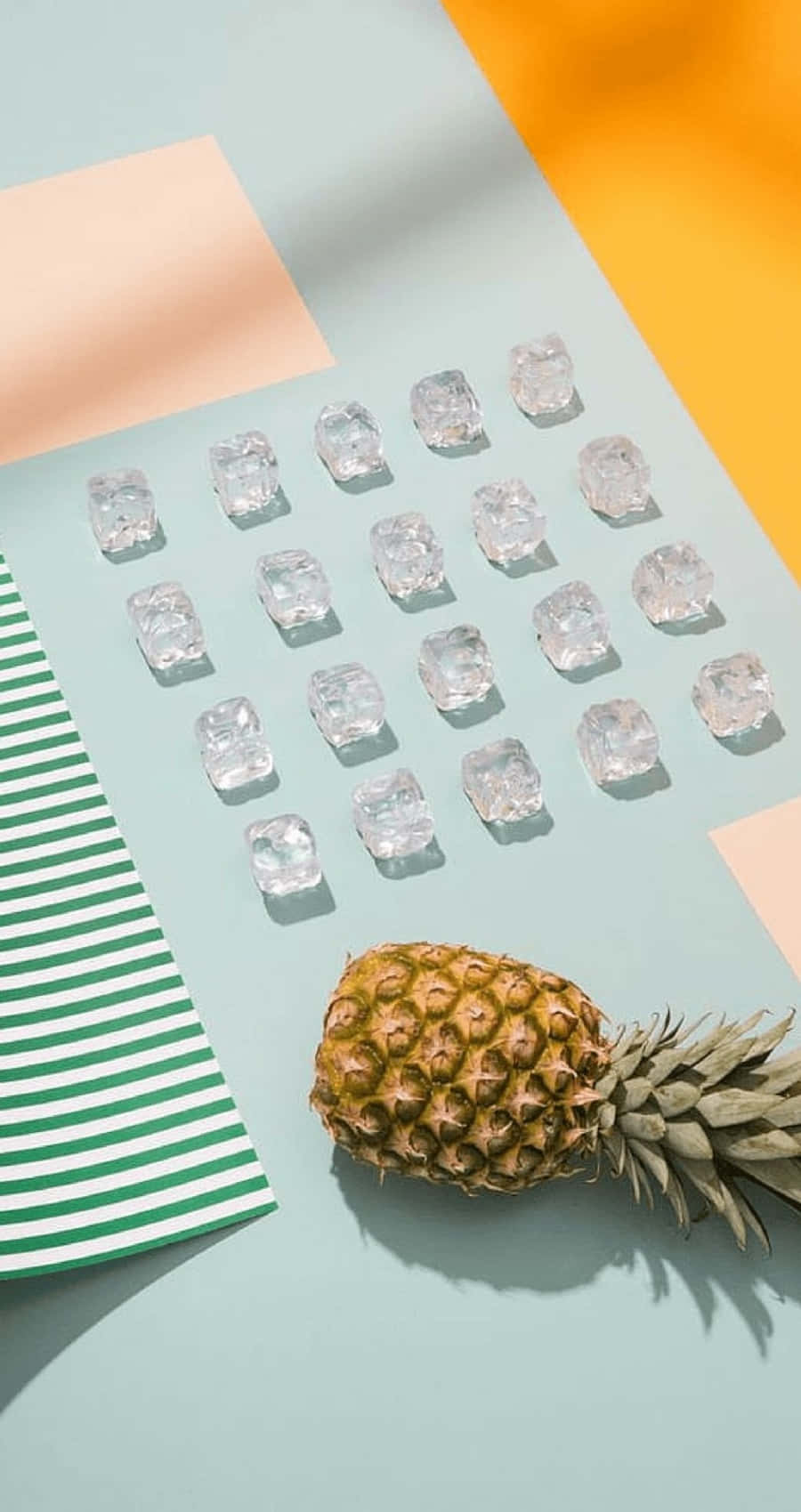 將你的iPhone升級至極致美學！ 壁紙 — 一個菠蘿放在冰塊網格旁邊，背景是粉彩色，帶有幾何色塊和條紋紙。