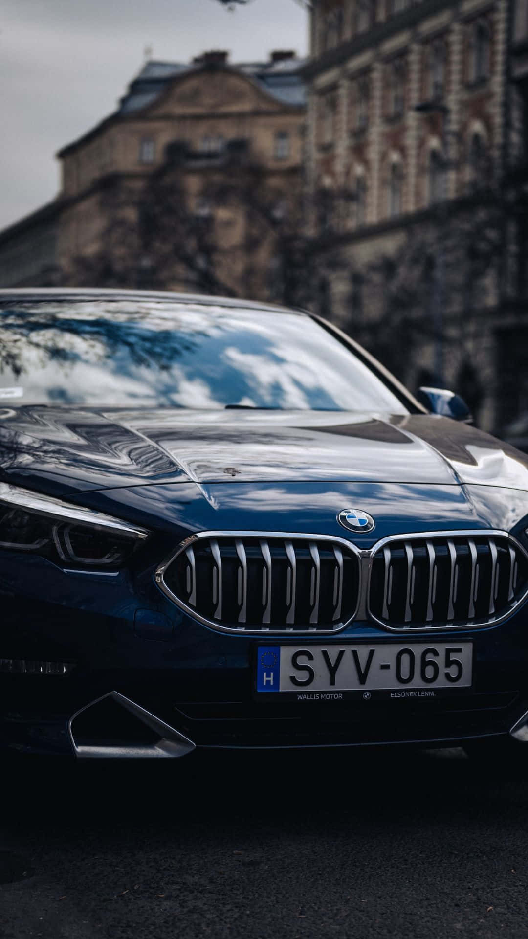 將您的BMW駕駛體驗提升至全新境界，配備創新安卓系統 壁紙 — 一輛時尚的深藍色BMW轎車停泊在城市的街道上，背景是歷史建築，天空多雲。
