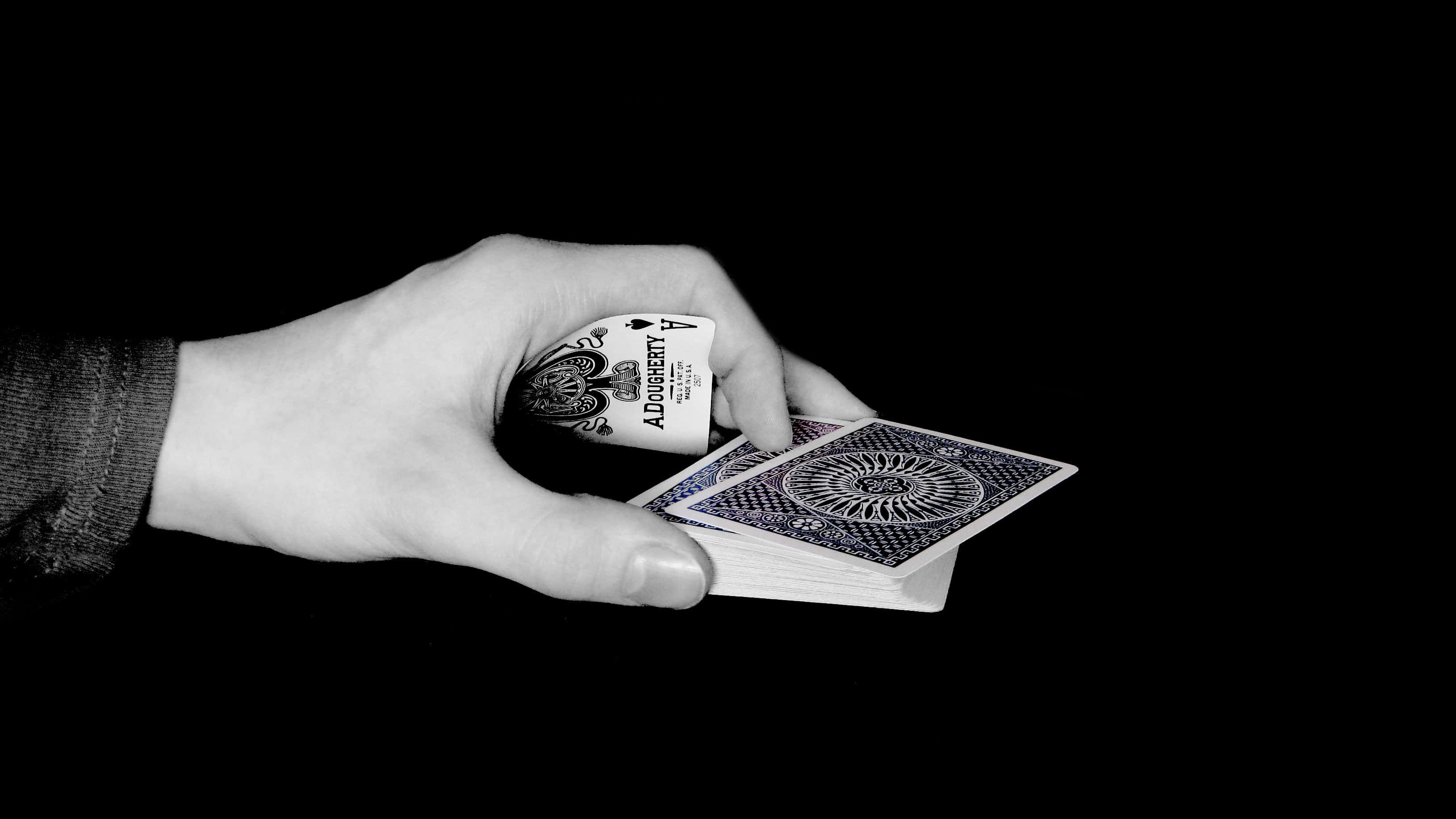 將撲克牌遊戲提升到新高度 壁紙 — 一隻手拿著一副啤牌，背景係純黑色，黑桃Ace露出嚟。