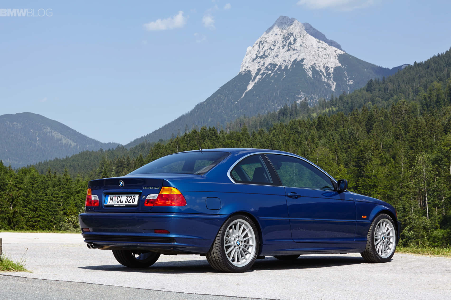 將極致駕馭機器納入生活 壁紙 — 一輛亮藍色BMW 328Ci雙門轎跑車停泊在道路上，背景是白雪覆蓋的山峰和茂密的森林，天空清澈湛藍。