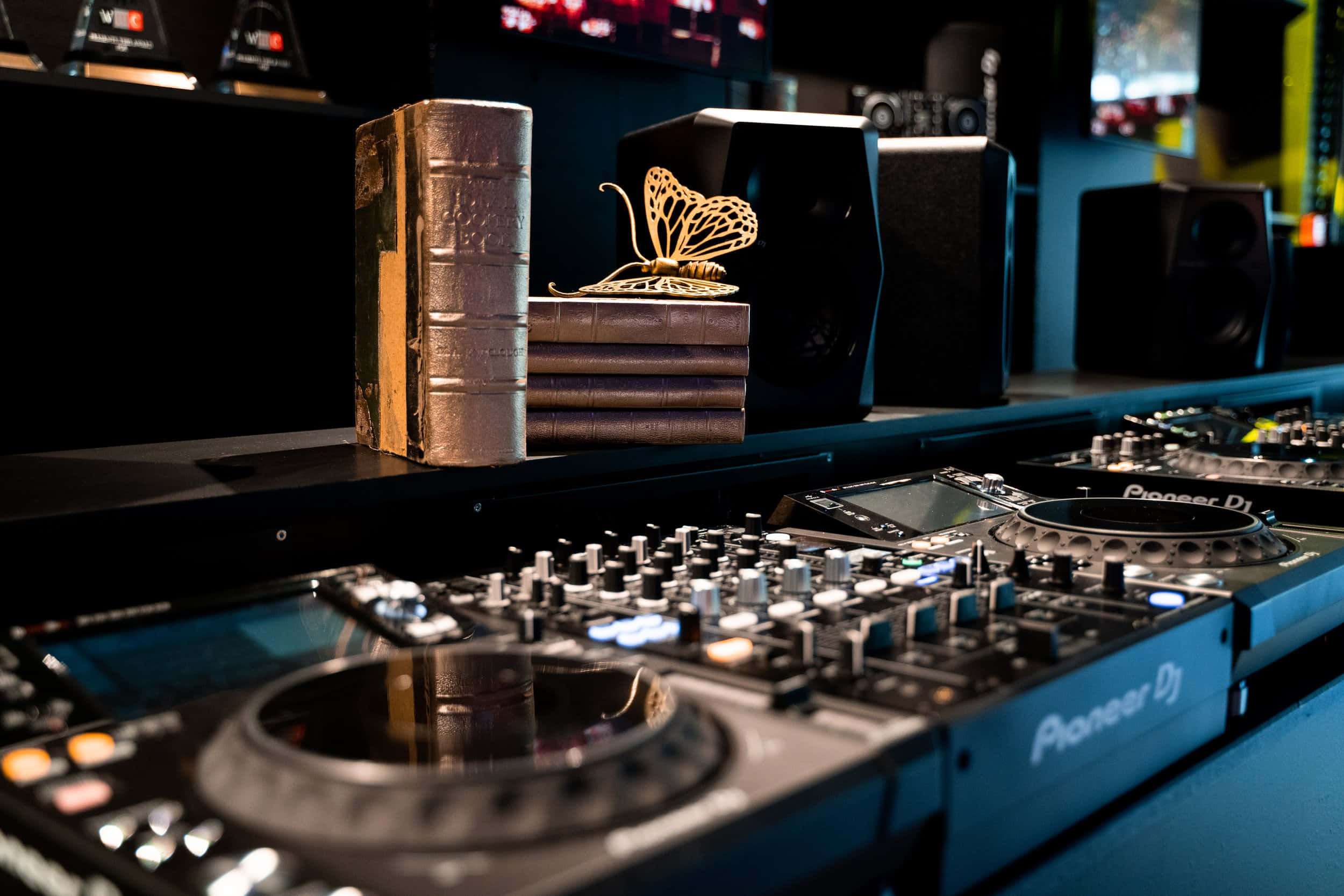 DJ 桌布 壁紙 — 專業DJ設備，配備Pioneer唱盤和控制器，在憂鬱的藍色燈光下，後方架上有復古書籍和蝴蝶雕塑。