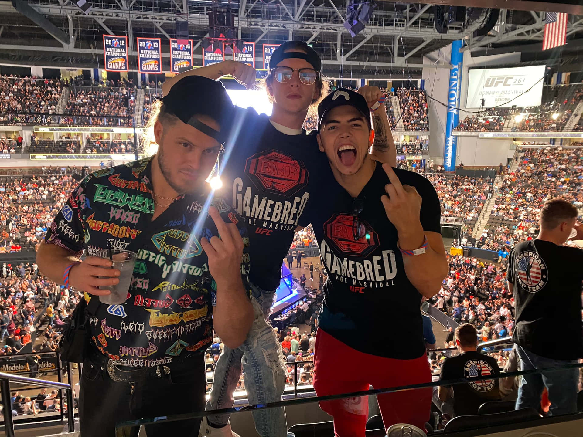 專業摔角手Sammy Guevara與Marko Stunt 壁紙 — 三名身穿UFC裝備的興奮粉絲在擠滿人的場館內，於現場混合武術比賽中舉起拳頭擺姿勢。