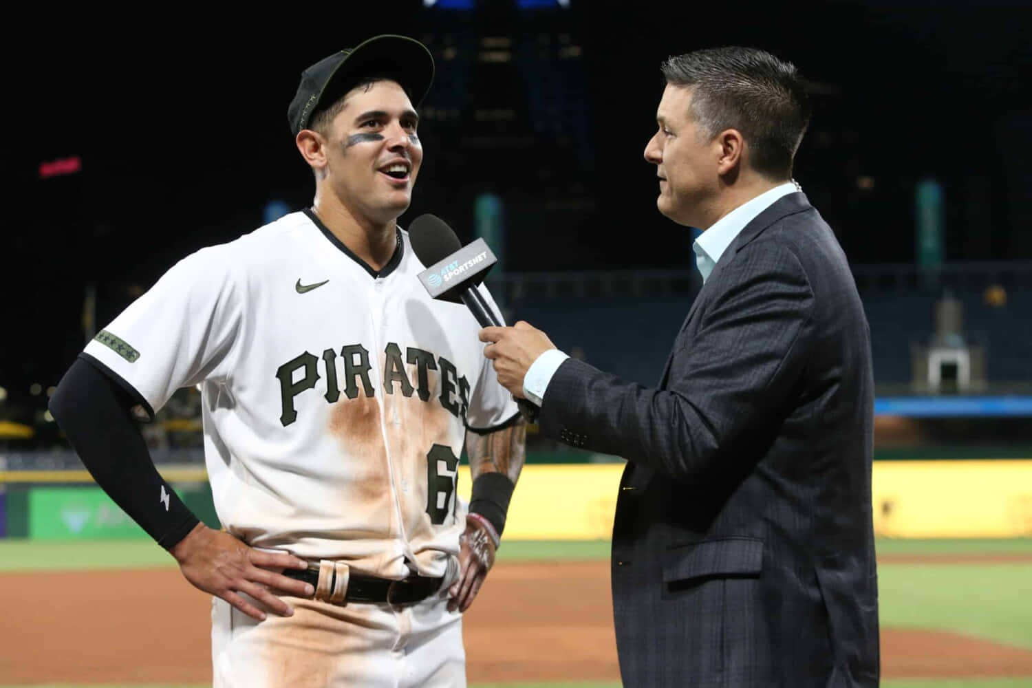 專業職業面試場景 壁紙 — 一名微笑的棒球選手穿著髒兮兮的 Pirates 制服，在夜晚的體育場上接受記者採訪。