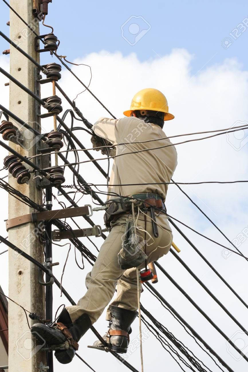 專業電工修復電柱 壁紙 — 一名戴著黃色頭盔的公用事業工人，在明亮的藍天下，攀爬一根被纏繞電線包圍的風化木電線桿。