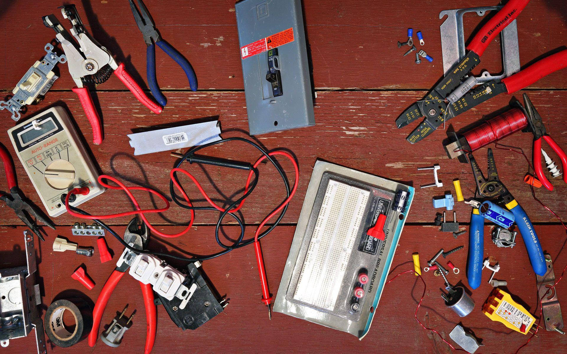 專業電工工具與設備 壁紙 — 從上方俯瞰各種電動工具和零件散落在風化的紅色木製工作台上。