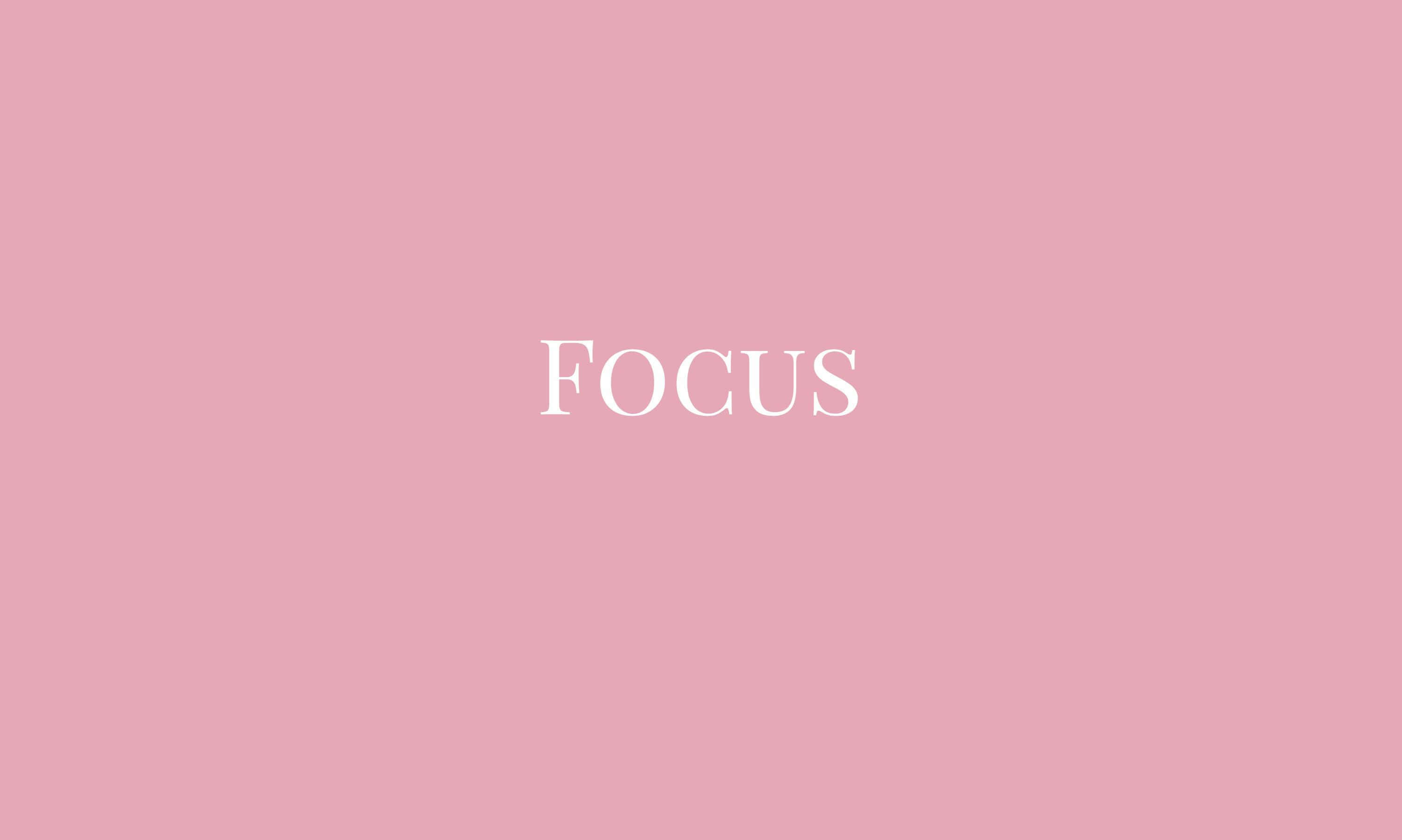 專注桌面粉紅美學 壁紙 — 優雅的白色襯線字體「focus」一詞居中顯示在柔和的粉紅色背景上。