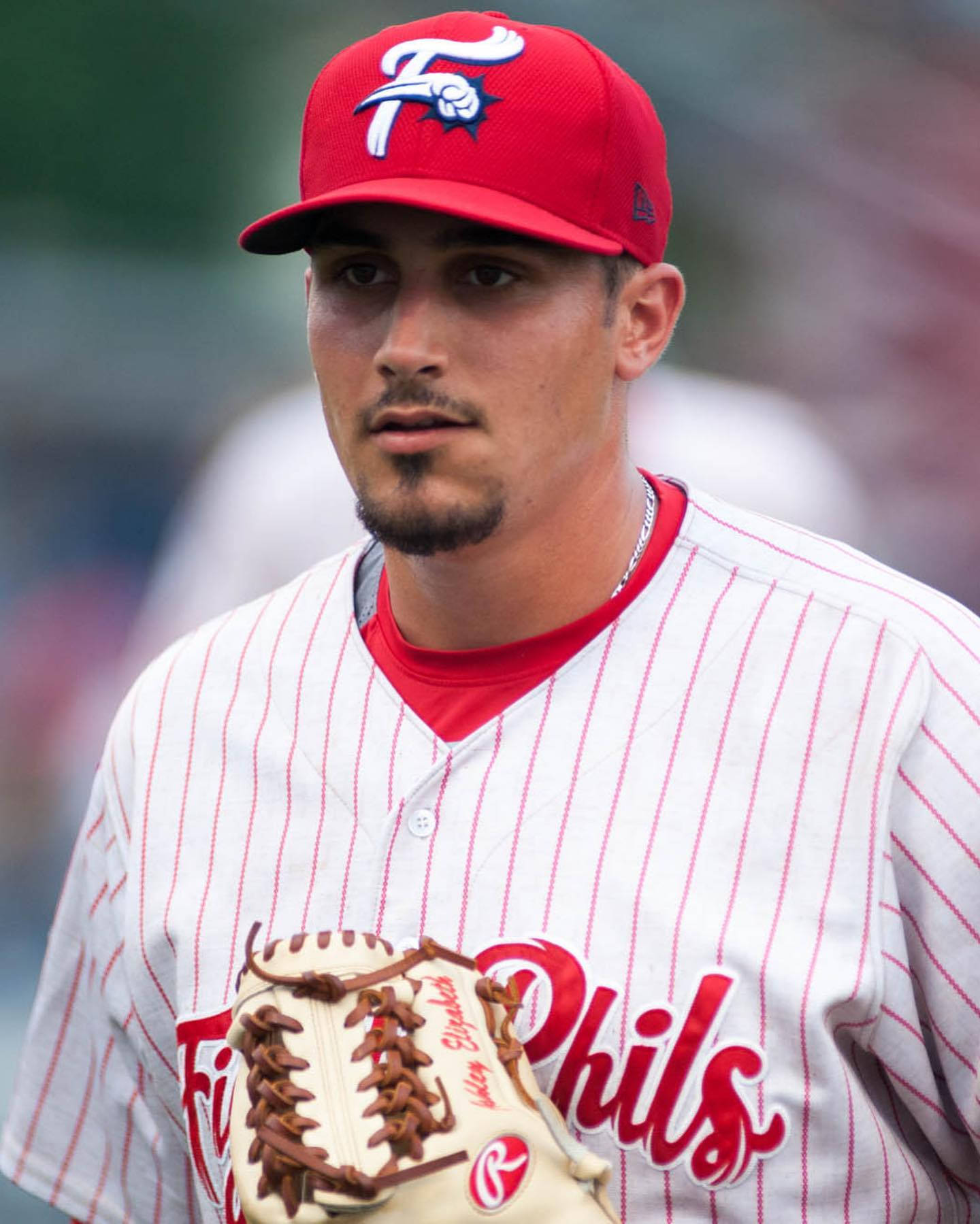 專注的投手Zach Eflin 壁紙 — 一位專注的棒球運動員身穿紅白條紋制服，戴著帶有風格化「F」標誌的紅色帽子，手持手套。