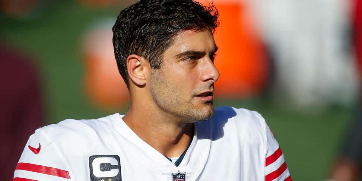 Jimmy Garoppolo 桌布 壁紙 — 專注的足球員身穿白色紅條紋球衣並佩戴隊長臂章，在明亮日光下的特寫。