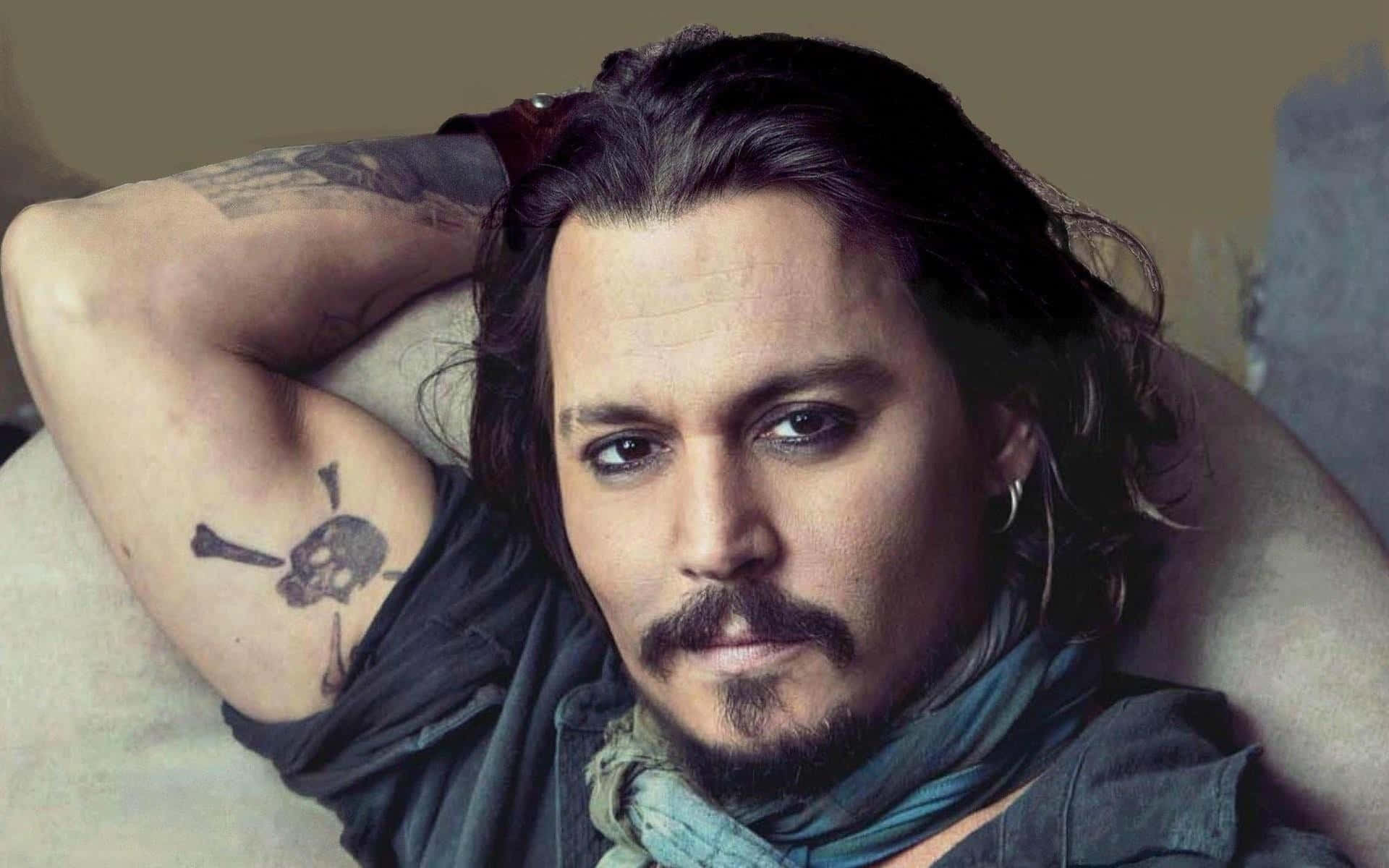 Johnny Depp 桌布 壁紙 — 尊尼特普留著深色長髮，有骷髏紋身，將頭靠在手臂上，專注地凝視鏡頭。