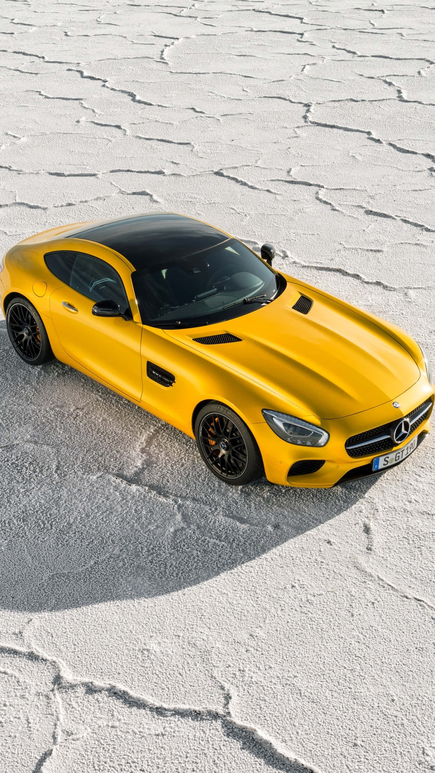 尊貴Android AMG GT-R高畫質壁紙 壁紙 — 一輛鮮黃色的Mercedes-AMG GT跑車，配備黑色車頂和輪圈，停在龜裂的鹽灘上，在明亮的日光下。
