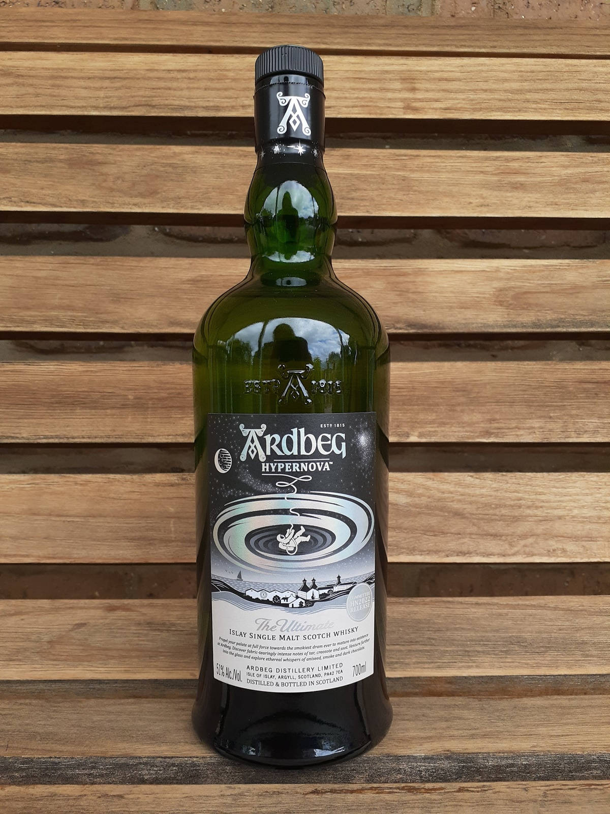 木條上的綠色Ardbeg Hypernova威士忌瓶，帶有宇宙風格標籤設計。