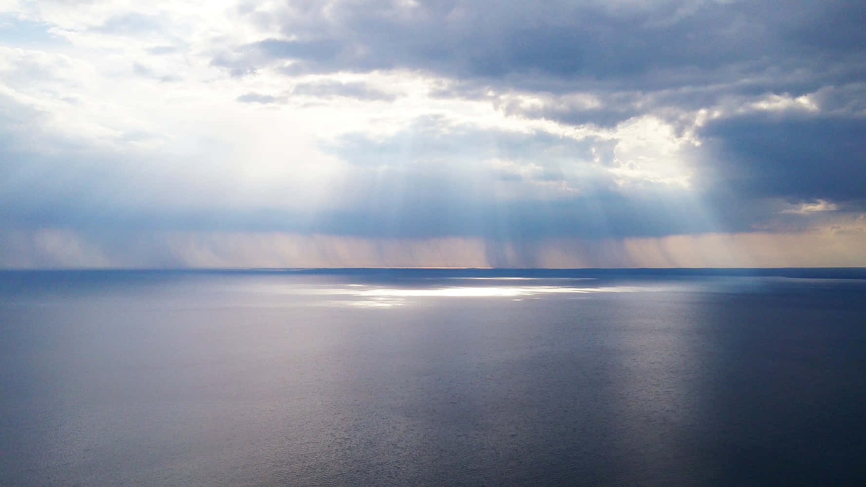 尋找內在寧靜 壁紙 — 陽光穿過暴風雲，在廣闊平靜的海洋地平線上投射出戲劇性的光線。