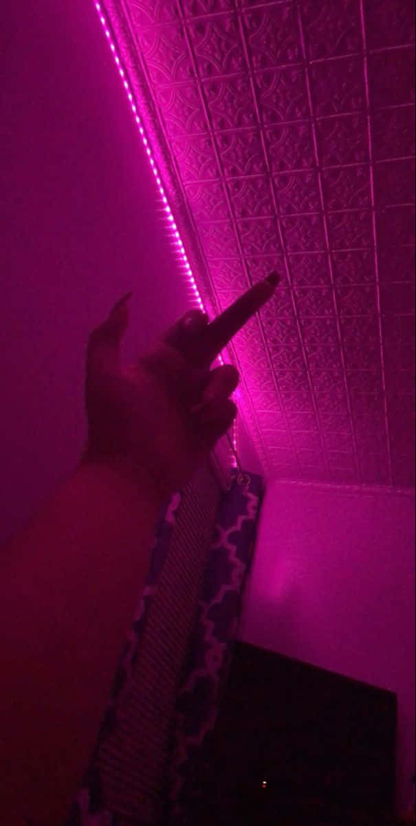 手指向有紋理天花板上的粉紅色LED燈帶照明。