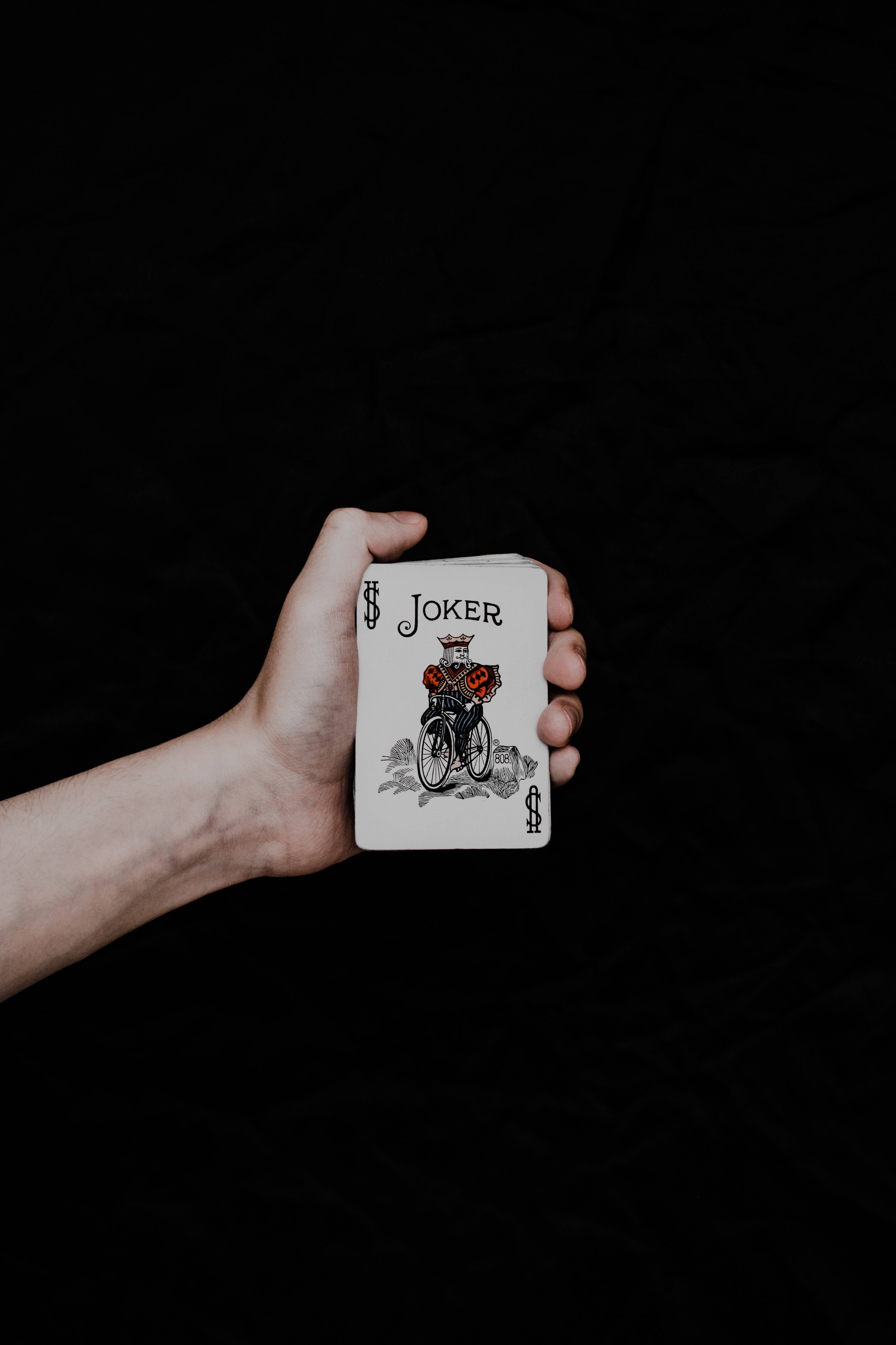 小丑 iPhone 牌子 壁紙 — 一隻手拿著一張小丑啤牌，背景是黑色紋理。