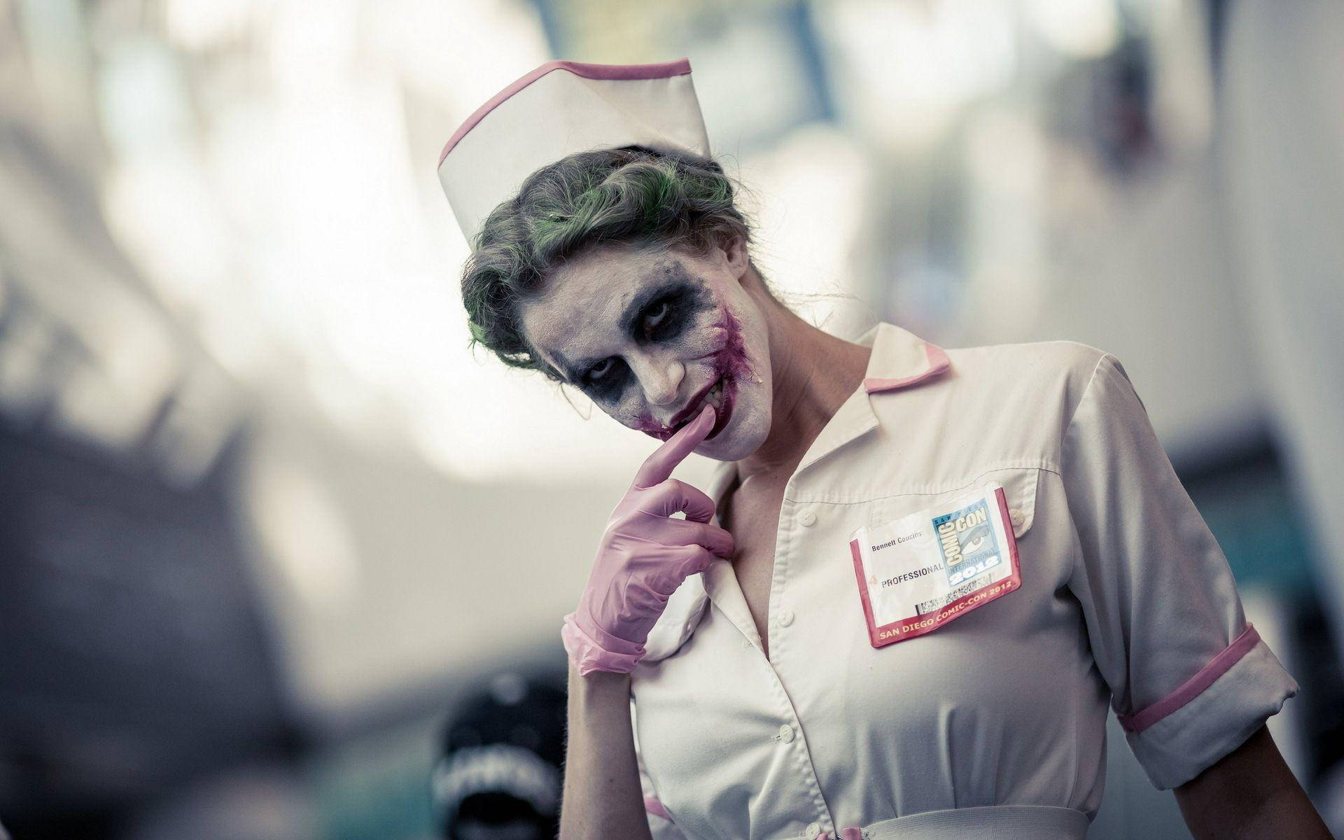 小丑女護士 壁紙 — 一位扮演小丑護士的cosplayer，綠色頭髮、白色臉部彩繪和粉紅色手套，手指放在嘴唇上擺姿勢。