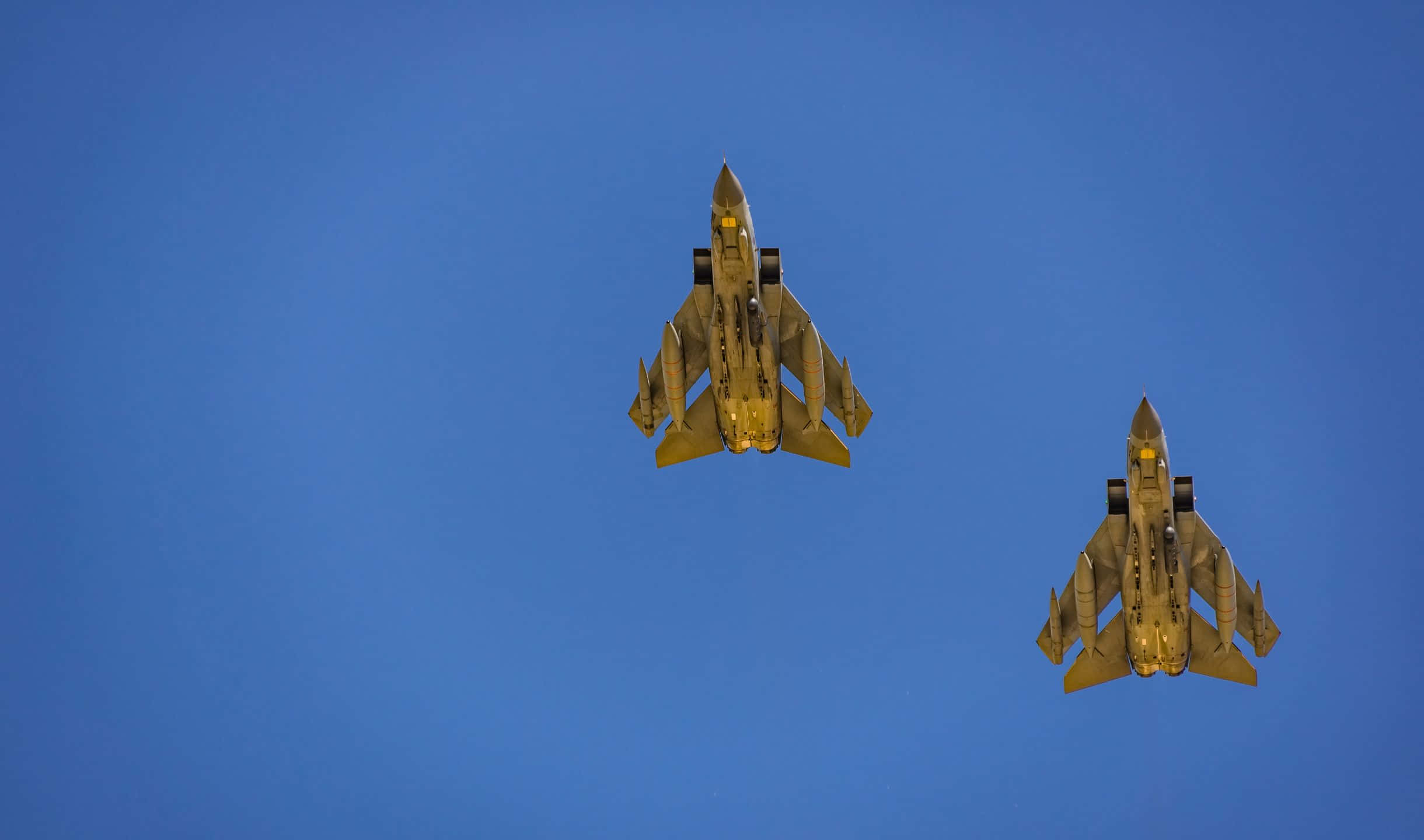小型私人飛機帶來的絕美飛行體驗 壁紙 — 兩架戰鬥機以編隊飛行，在清澈的藍天下，陽光在其金屬表面上閃閃發光。