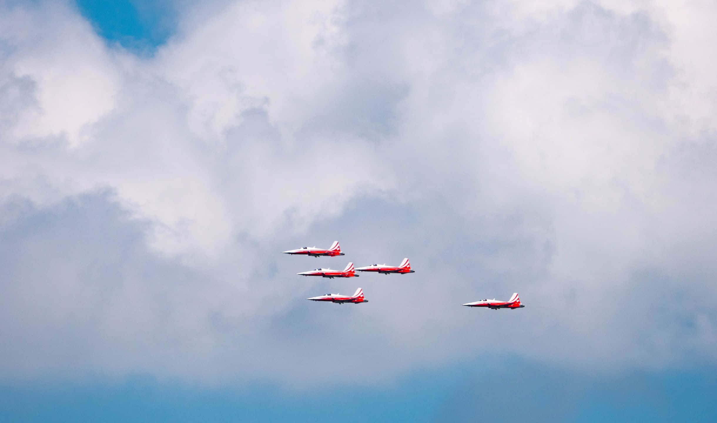 小型飛機在天空中翱翔的空中視角 壁紙 — 四架紅白相間的噴射機以緊密編隊飛行，穿過充滿蓬鬆白雲和藍色斑塊的戲劇性天空。