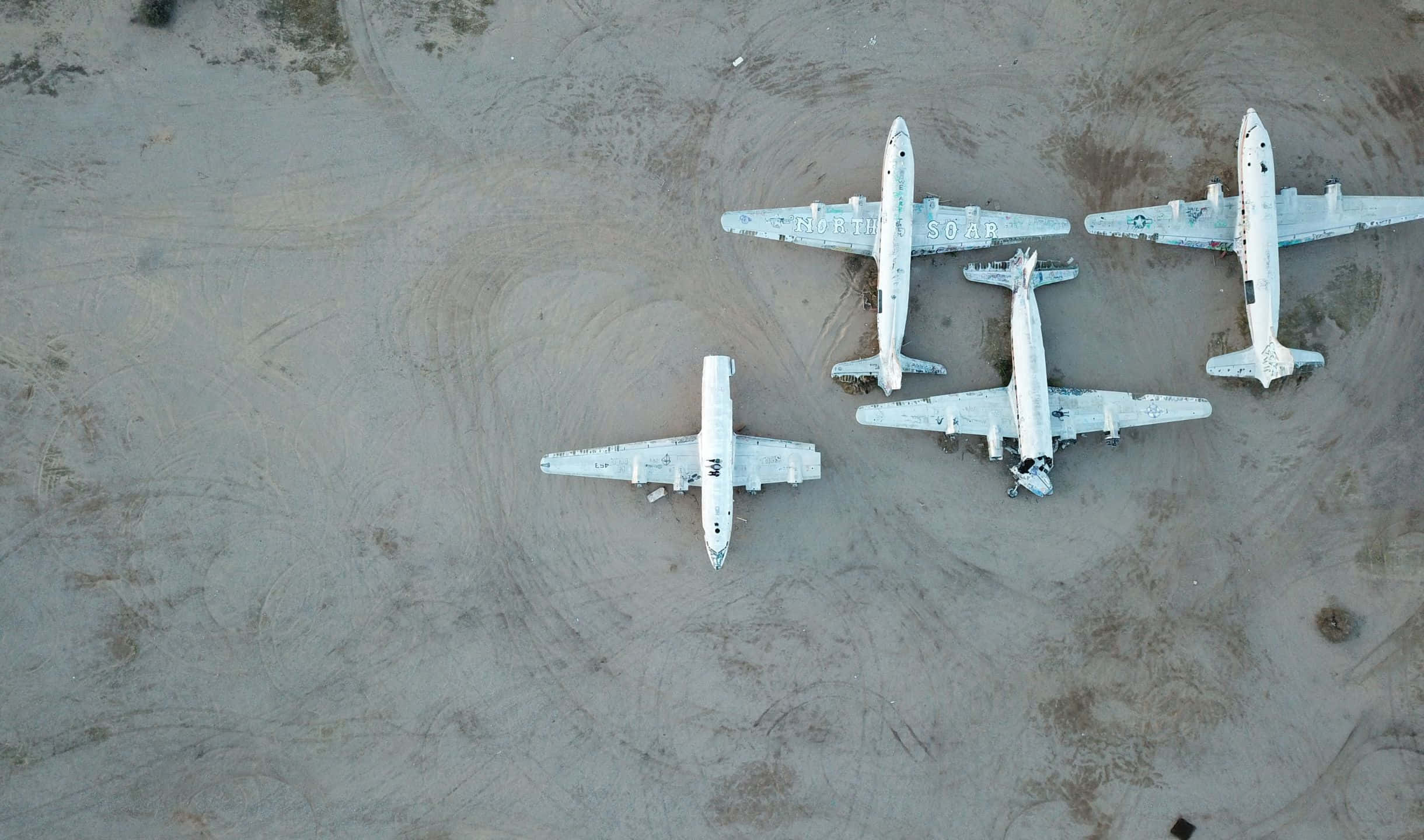 小型飛機翱翔雲層之上的空中視角 壁紙 — 鳥瞰四架白色復古飛機停泊在廣闊的沙質沙漠地面上。
