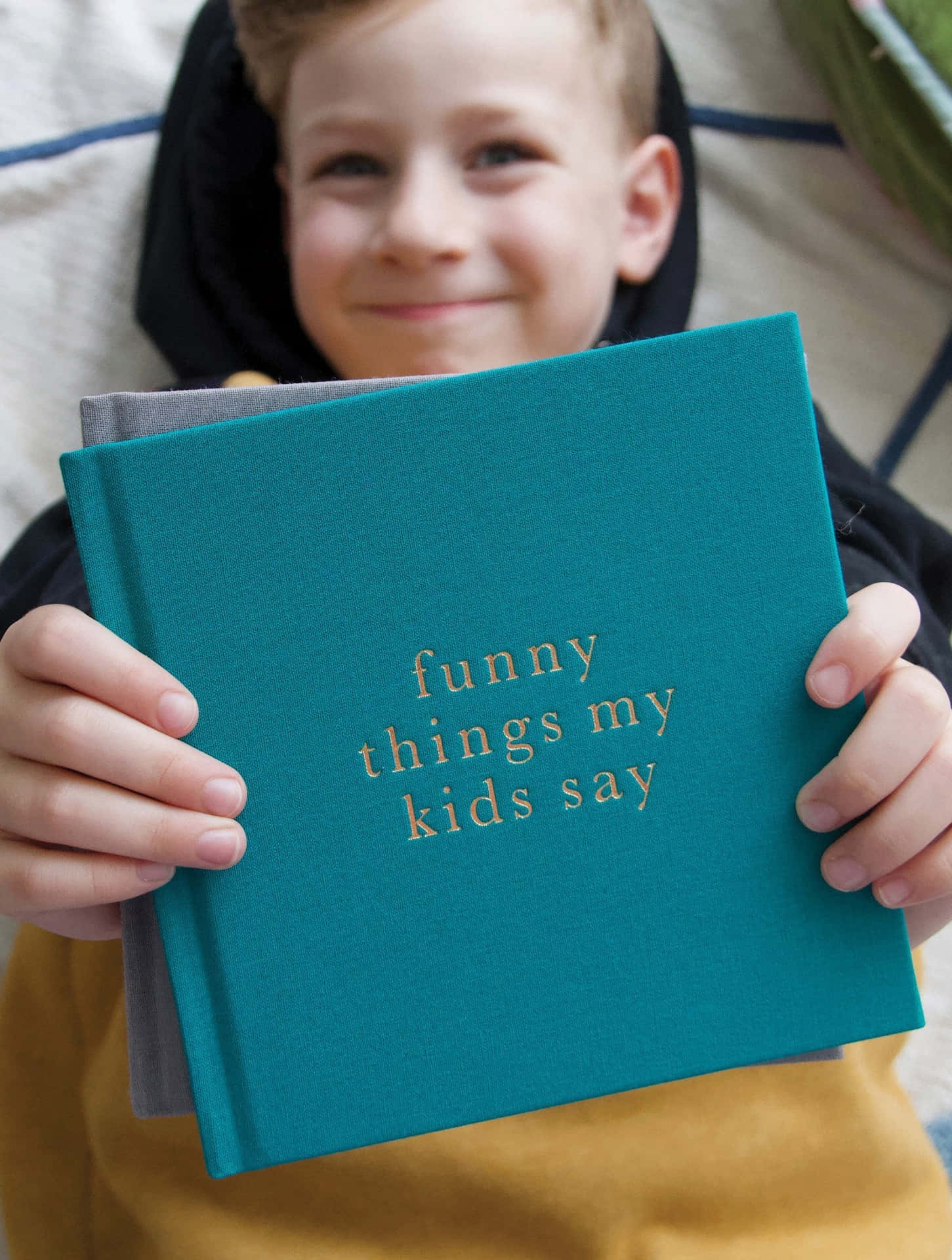 一個快樂的孩子拿著一本青綠色書，書名為 funny things my kids say。