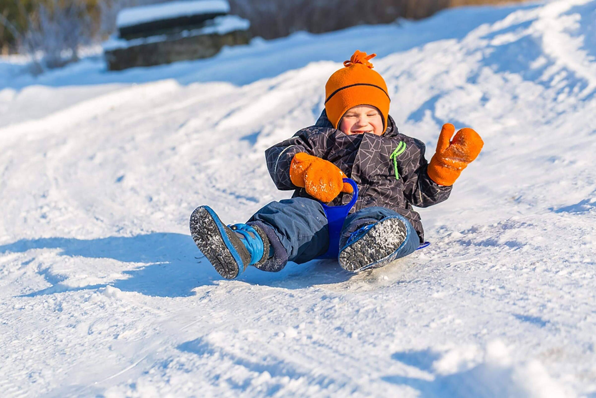 孩子戴著橙色帽子和手套從雪坡上滑雪橇