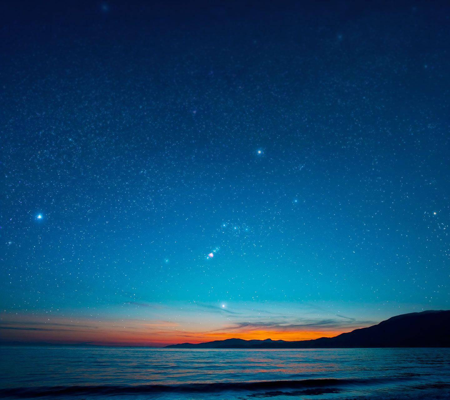 小米海洋夜空 壁紙 — 繁星點點的夜空在平靜的海洋上閃耀，遠山在火紅色的地平線上形成剪影。