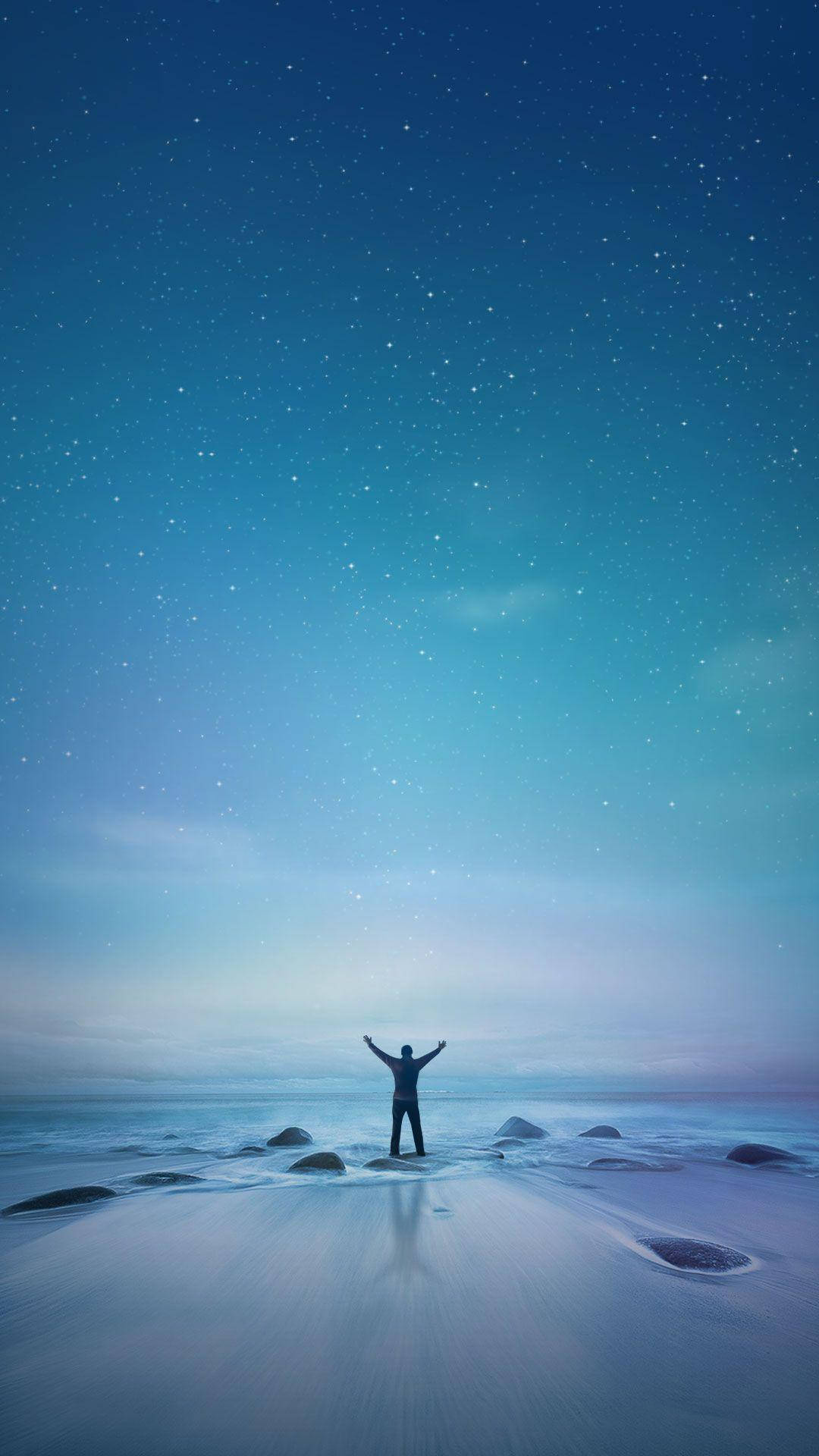 小米海灘男子 壁紙 — 一個孤獨的身影在星光閃爍的海灘上舉起雙臂，站在廣闊的漸變天空下。