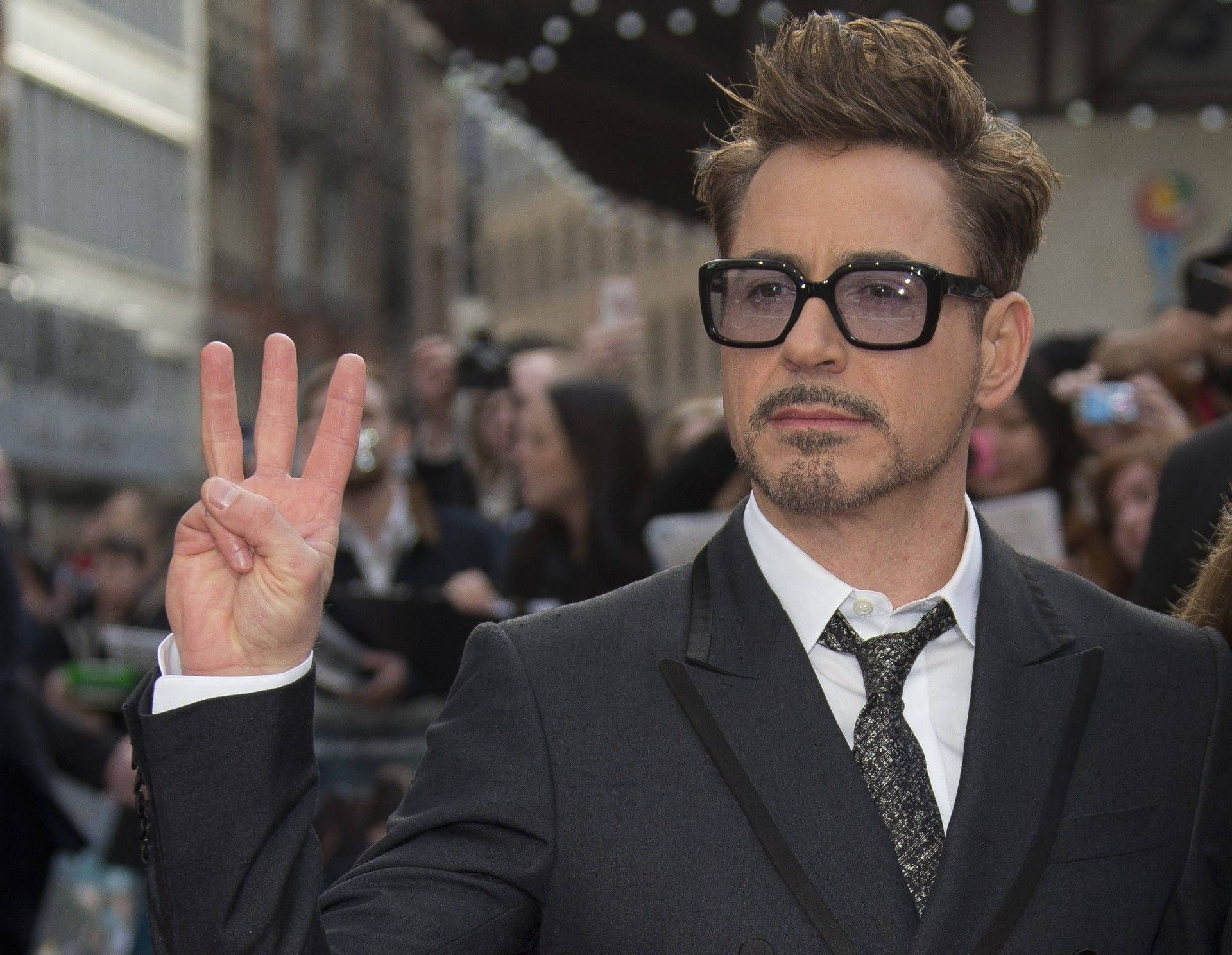 羅拔·唐尼（Robert Downey Jr.）身穿西裝和眼鏡在公開活動中比出和平手勢。