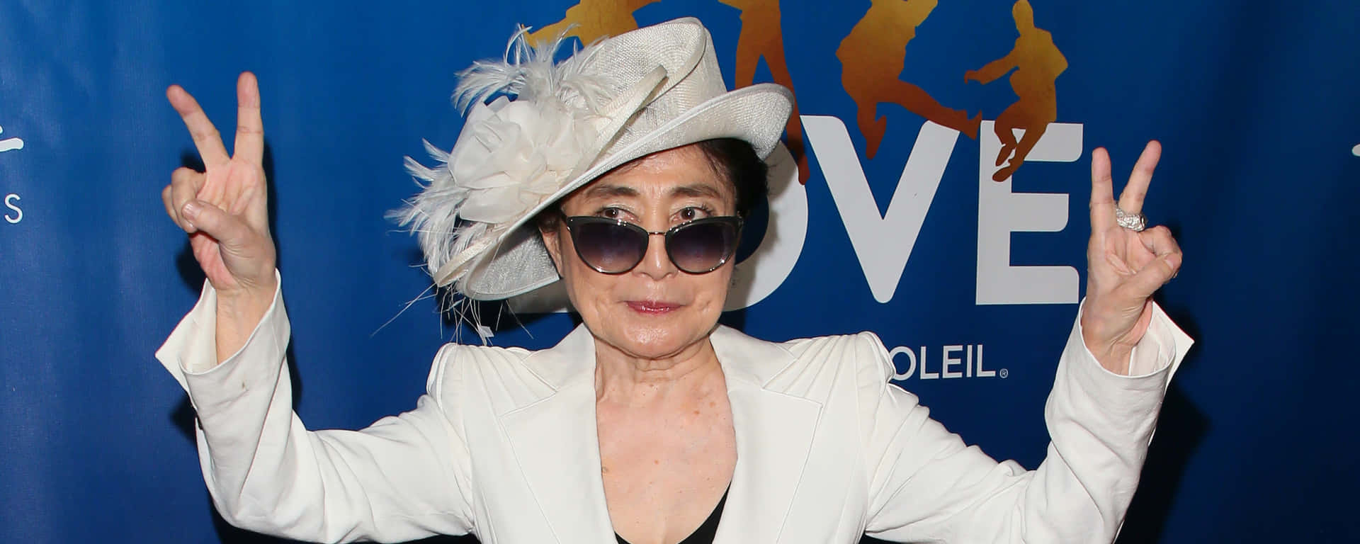 戴白色帽子和太陽眼鏡的女性在活動中比出和平手勢。
