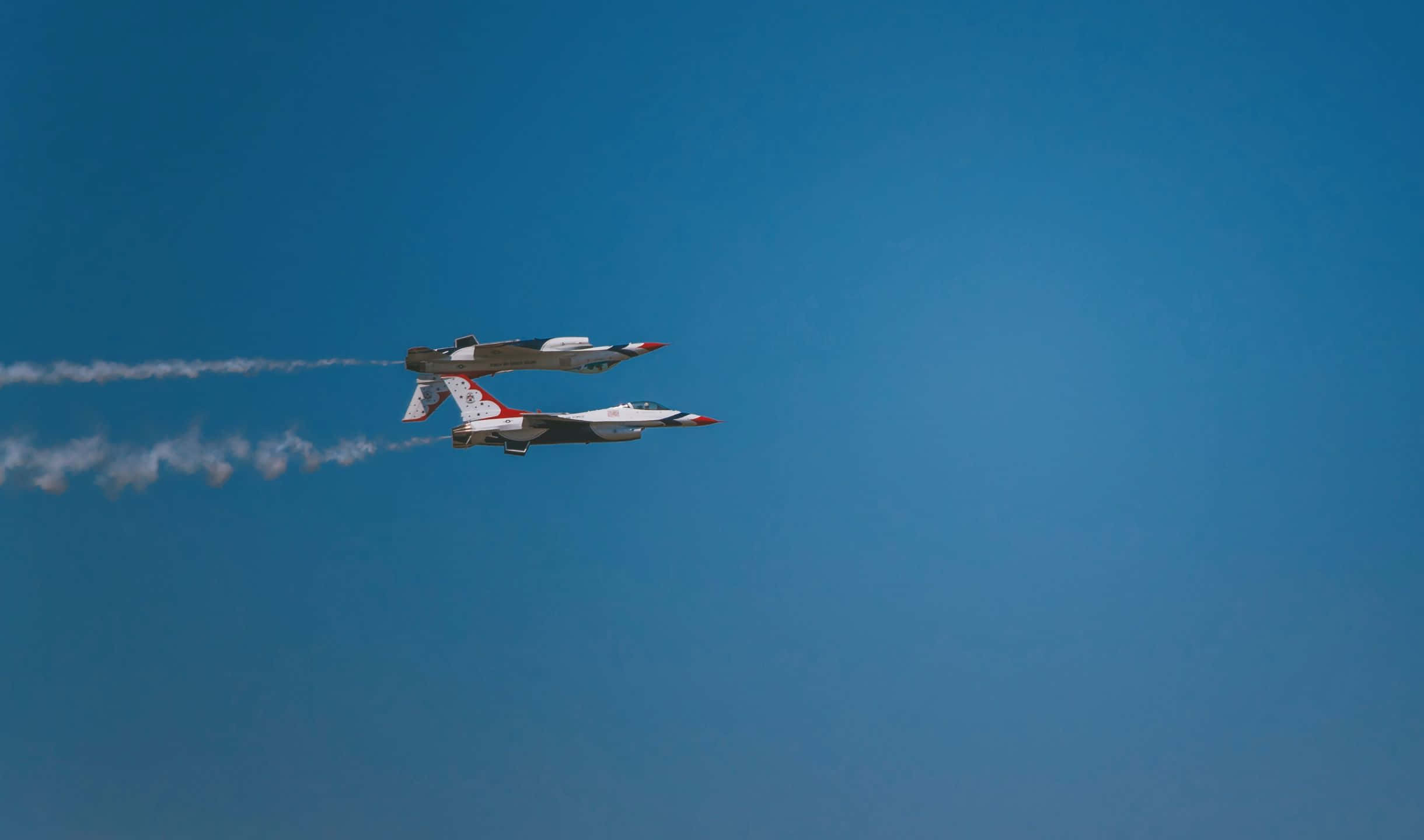 小飛機翱翔雲層之上 壁紙 — 兩架戰鬥機以緊密編隊飛行，在清澈的藍天中留下白色煙霧痕跡。