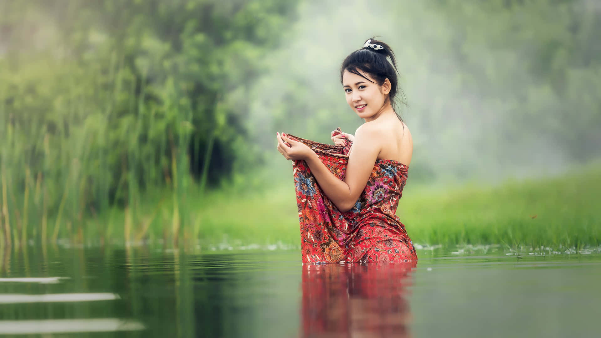 身穿圖案連衣裙的女子站在水中，背景有綠色蘆葦和霧氣。