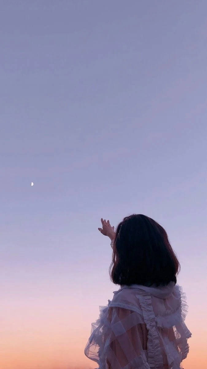 少女指月晴空手機壁紙 壁紙 — 一個穿著荷葉邊白色襯衫的人，向著融合紫色和桃色的暮色天空中的新月伸手。