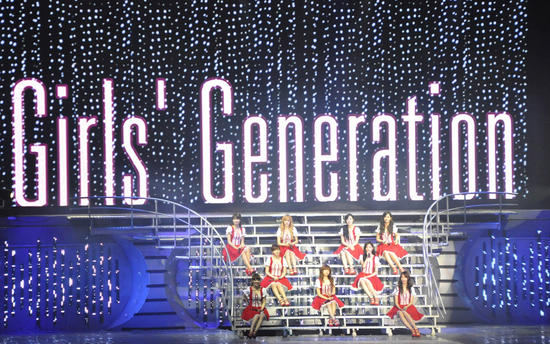 K-pop 組合少女時代穿著紅色服裝在發光的舞台上表演。