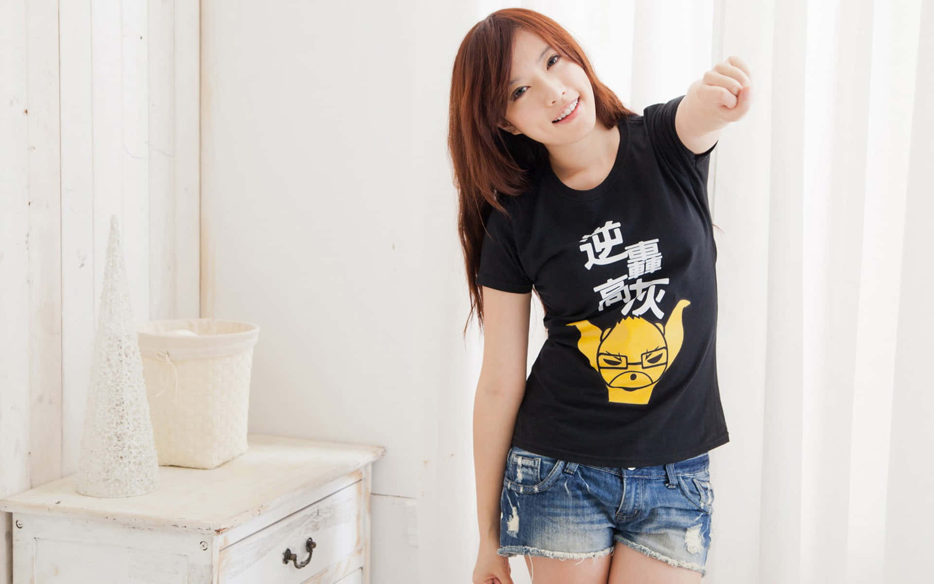 年輕女性穿著黑色T恤，帶有黃色卡通和中文文字，在室內微笑。