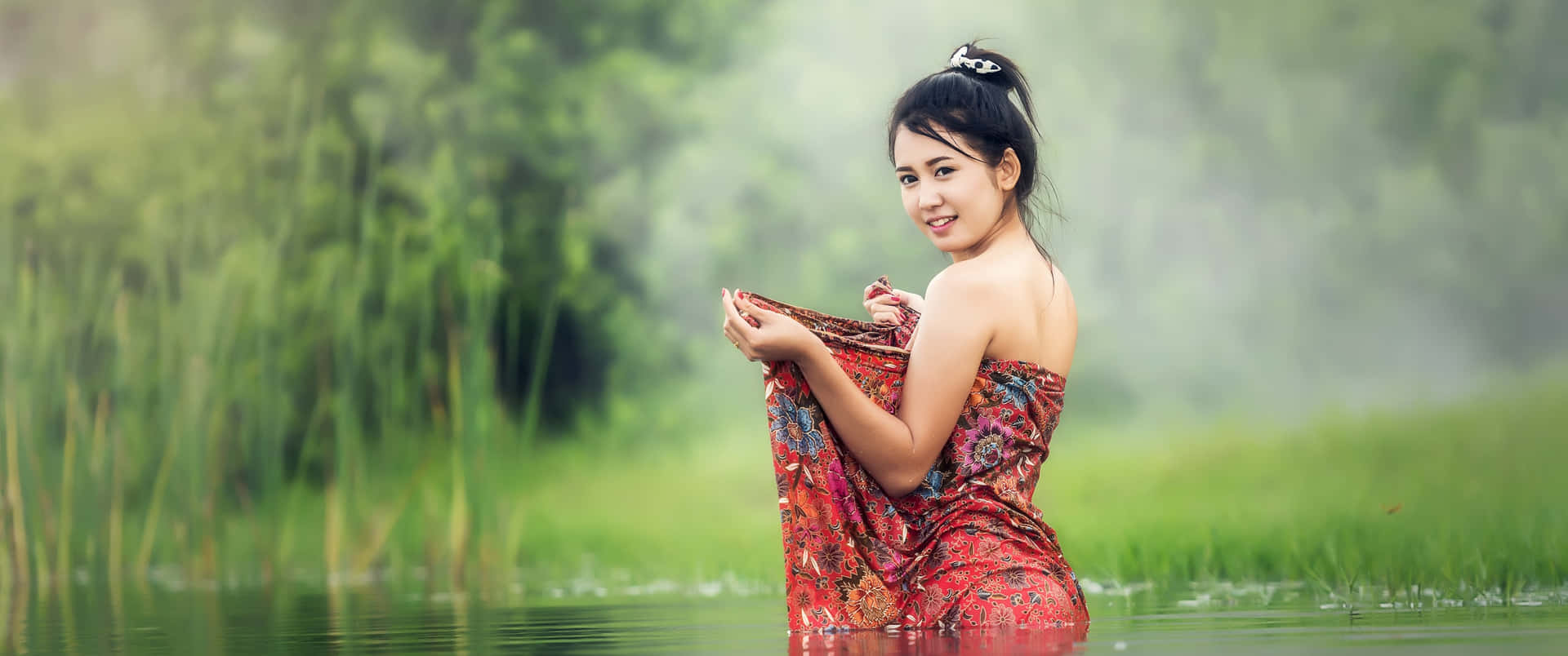 身穿紅色圖案連衣裙的女子站在霧氣瀰漫的綠色池塘中