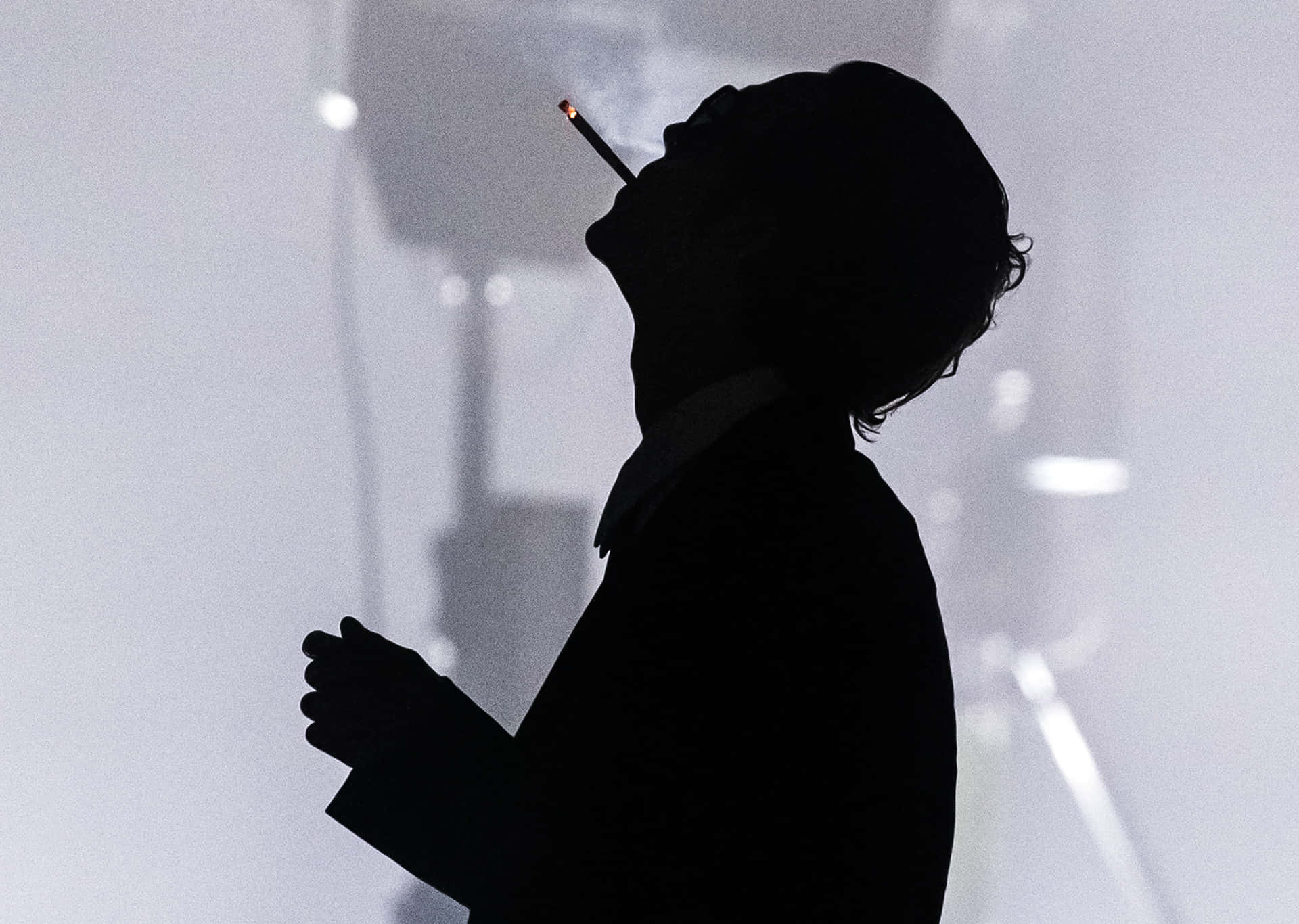 少年日常的甜美瞬間 壁紙 — 一個人在朦朧明亮背景中吸煙的剪影，帶有柔和發光的燈光。