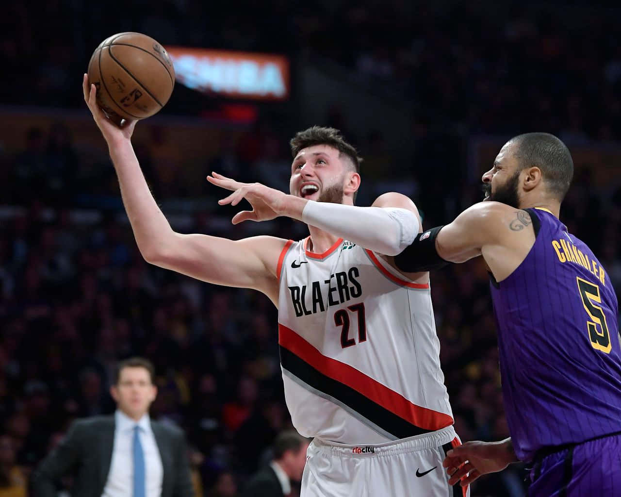 尤素福·努爾基奇與泰森·錢德勒 壁紙 — 一名身穿白色 Blazers 球衣的籃球運動員在擠滿觀眾的場館內投籃，同時受到一名身穿紫色球衣的對手防守。