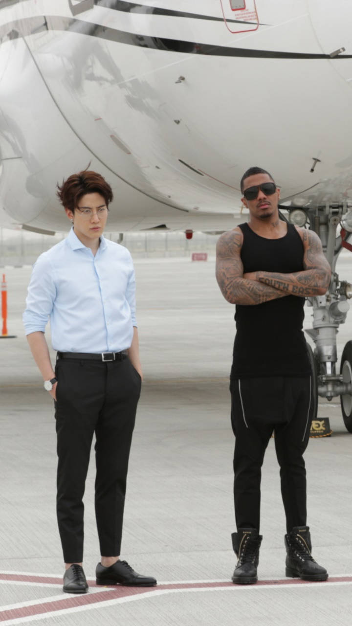 兩個男人在機場停機坪上靠近私人飛機擺姿勢，一個穿著正式服裝，另一個穿著帶有紋身的休閒黑色服裝。