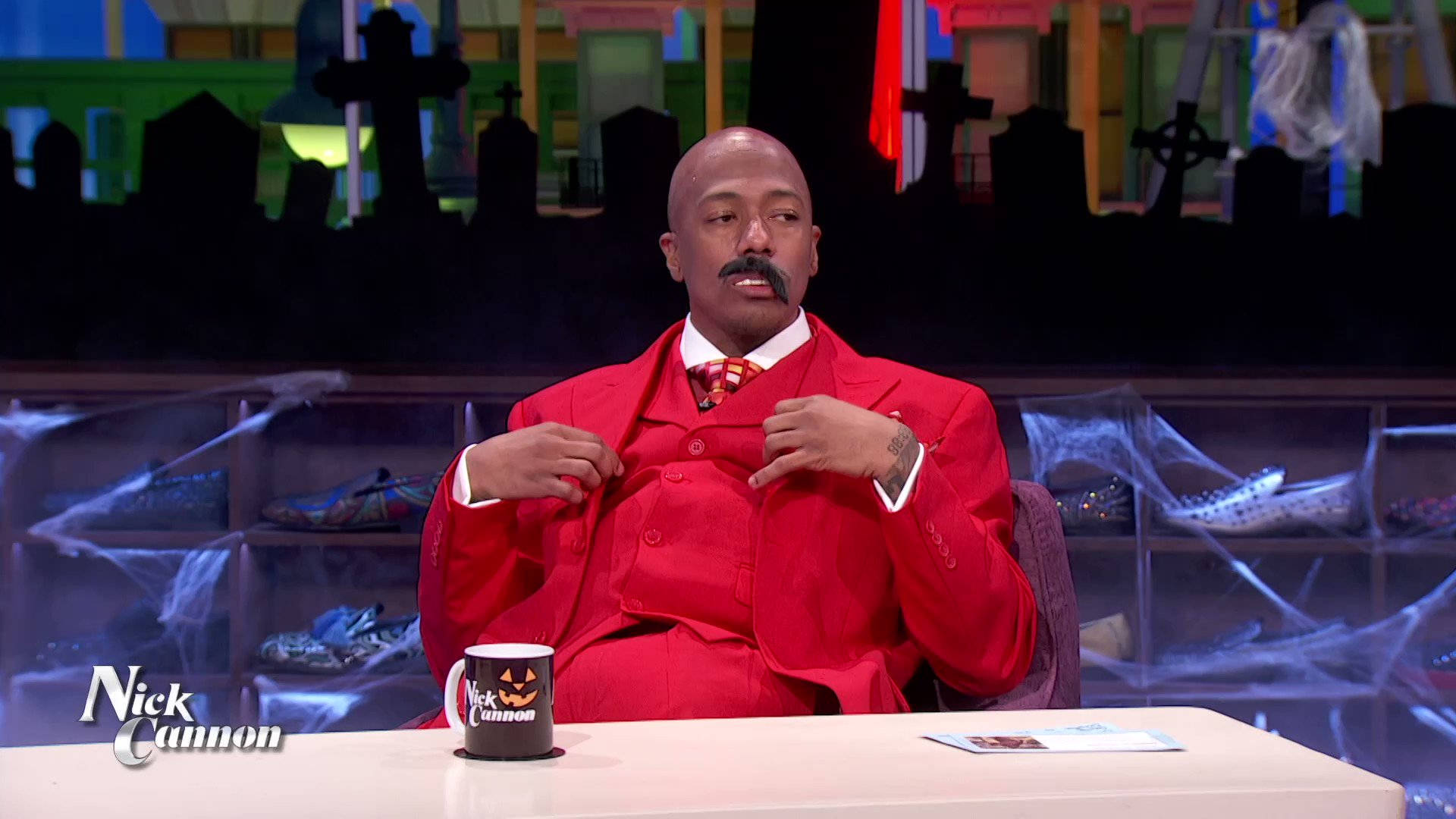 Nick Cannon 身穿紅色西裝主持萬聖節主題電視節目。
