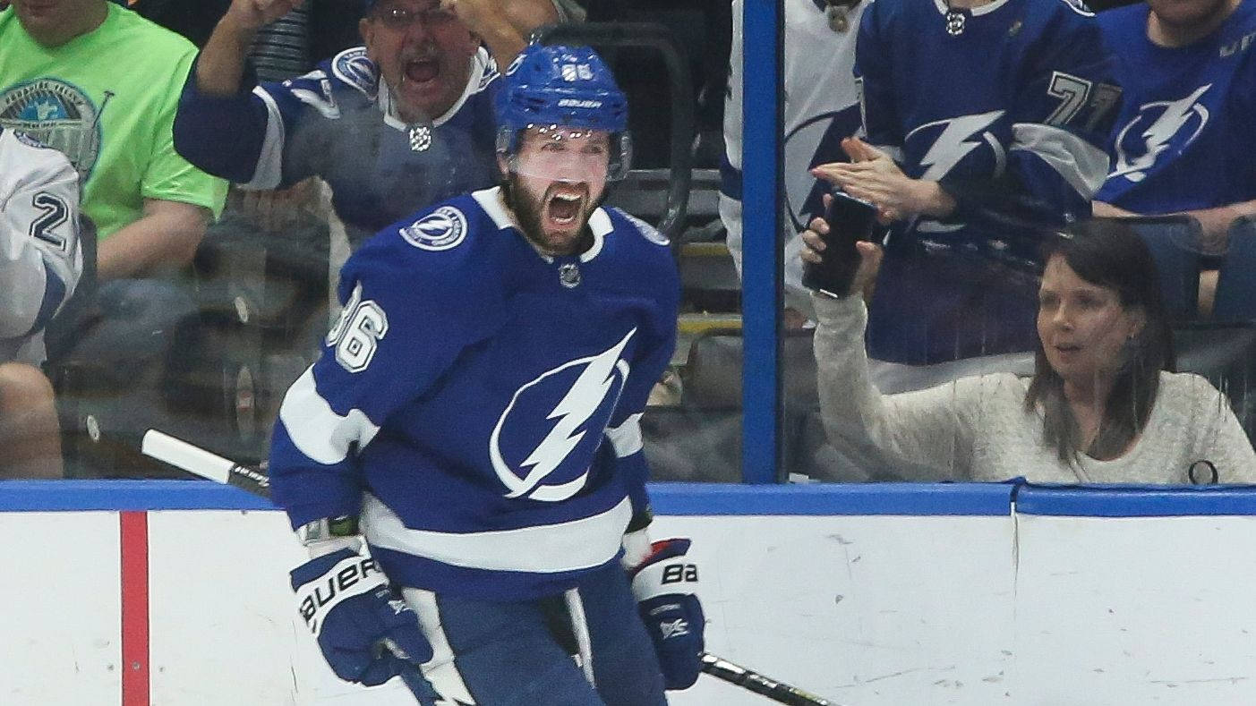 尼基塔·庫察羅夫 - NHL球員 壁紙 — 一位身穿藍色球衣的坦帕灣閃電冰球球員在冰上勝利咆哮，球迷在玻璃後歡呼。